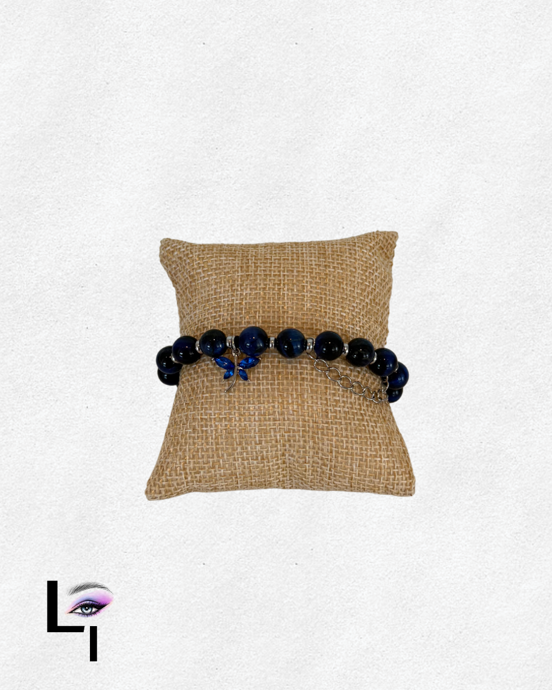 Black and blue beaded bracelet with a small charm, displayed on a tan woven pillow.