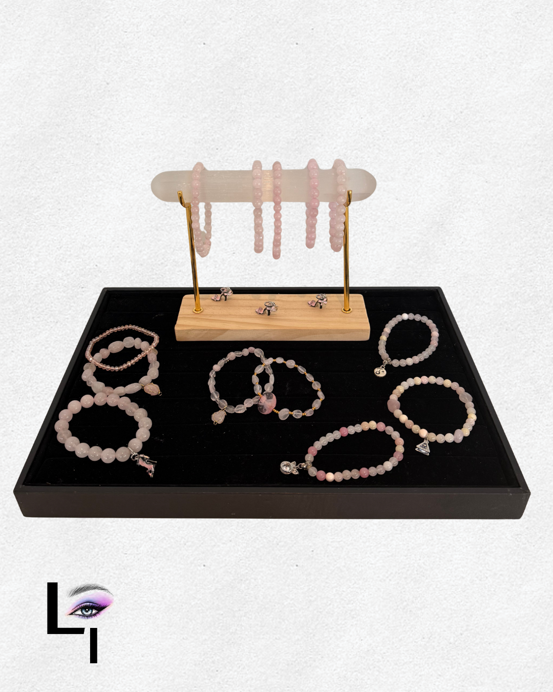 Display of pink and white beaded jewelry including bracelets, necklaces, earrings, and rings on a black tray and jewelry stand.