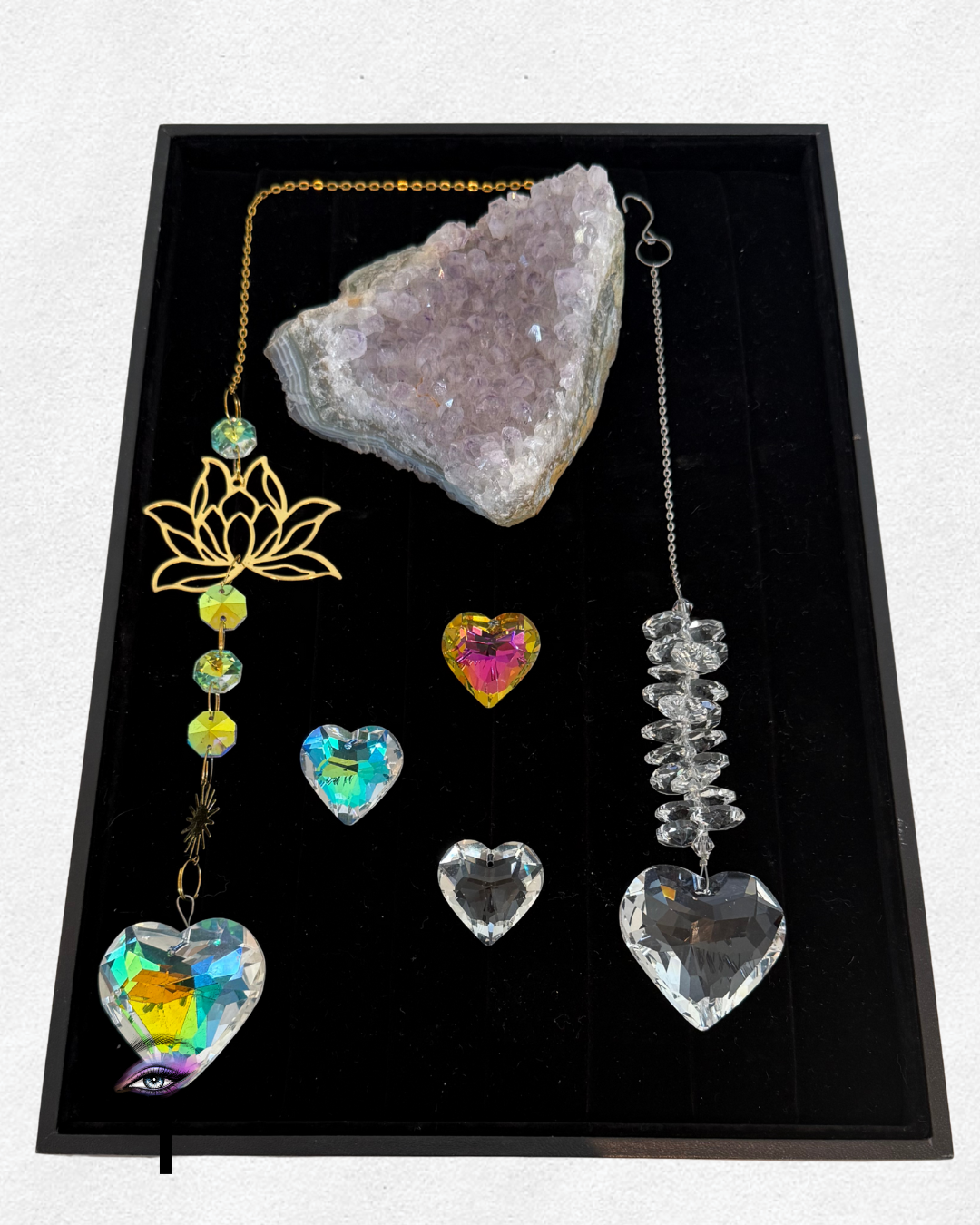 Jewelry box containing colorful crystal necklaces and heart-shaped crystals, with a large raw amethyst geode in the center.