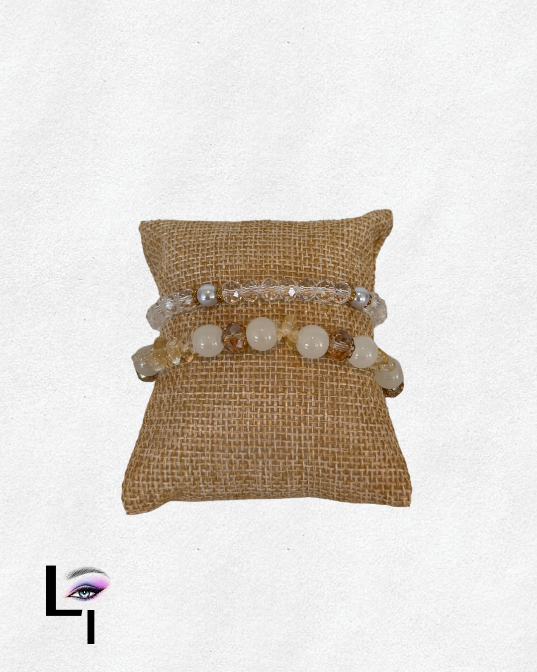 Three beaded bracelets displayed on a small, textured beige cushion.