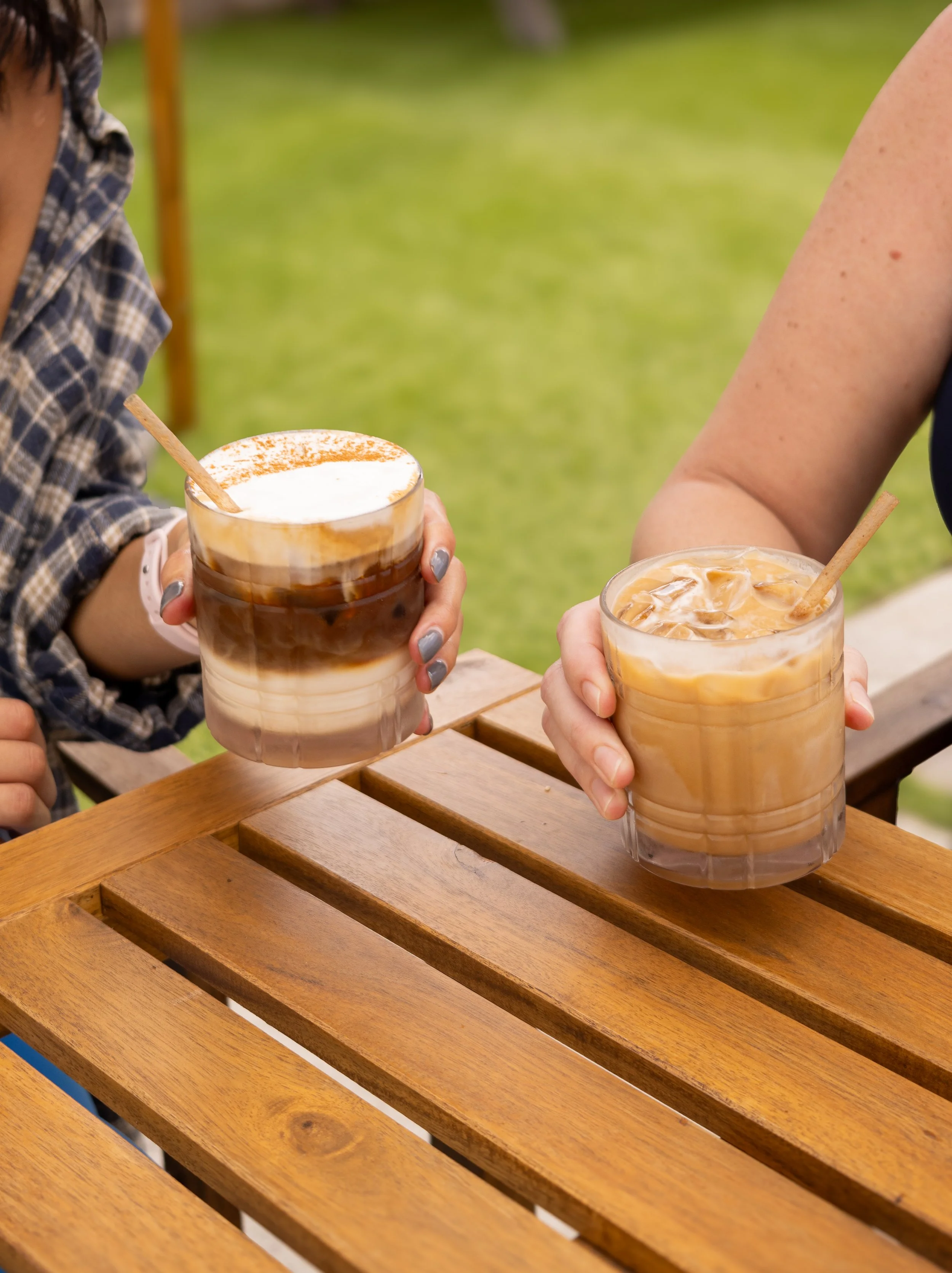 Small business brand photography in Tampa. Small business branding. Visual branding. Two people holding iced coffee drinks in glasses, sitting at a wooden table outdoors.