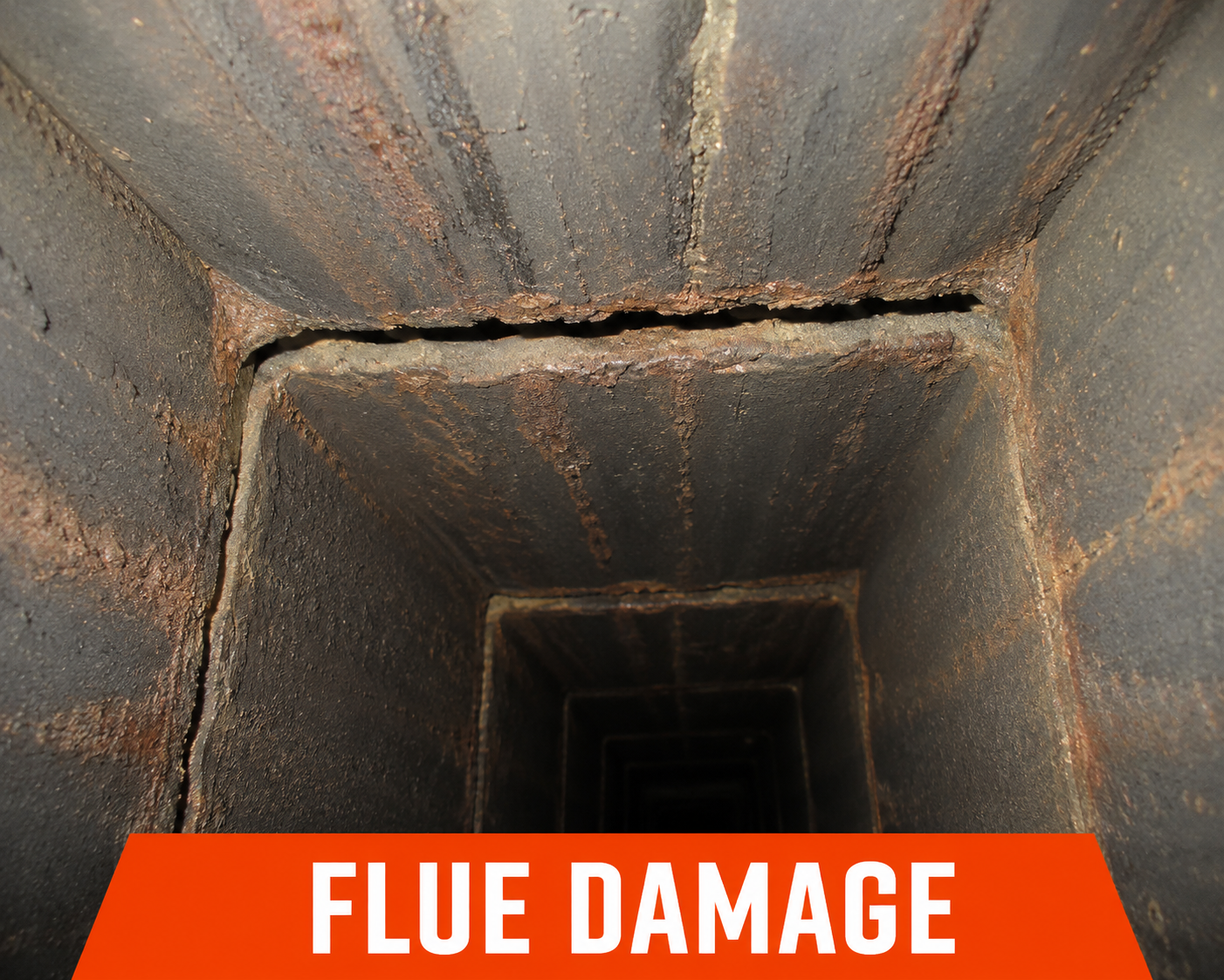 A vertical view down into a rusty flue or chimney with visible damage to the brick lining, indicating flue damage.