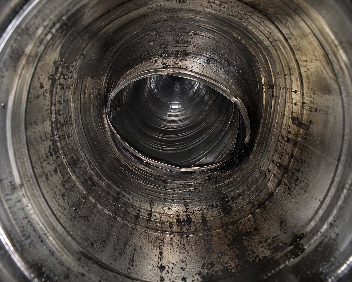 Close-up of a metallic industrial pipe interior with grime and oil residue.