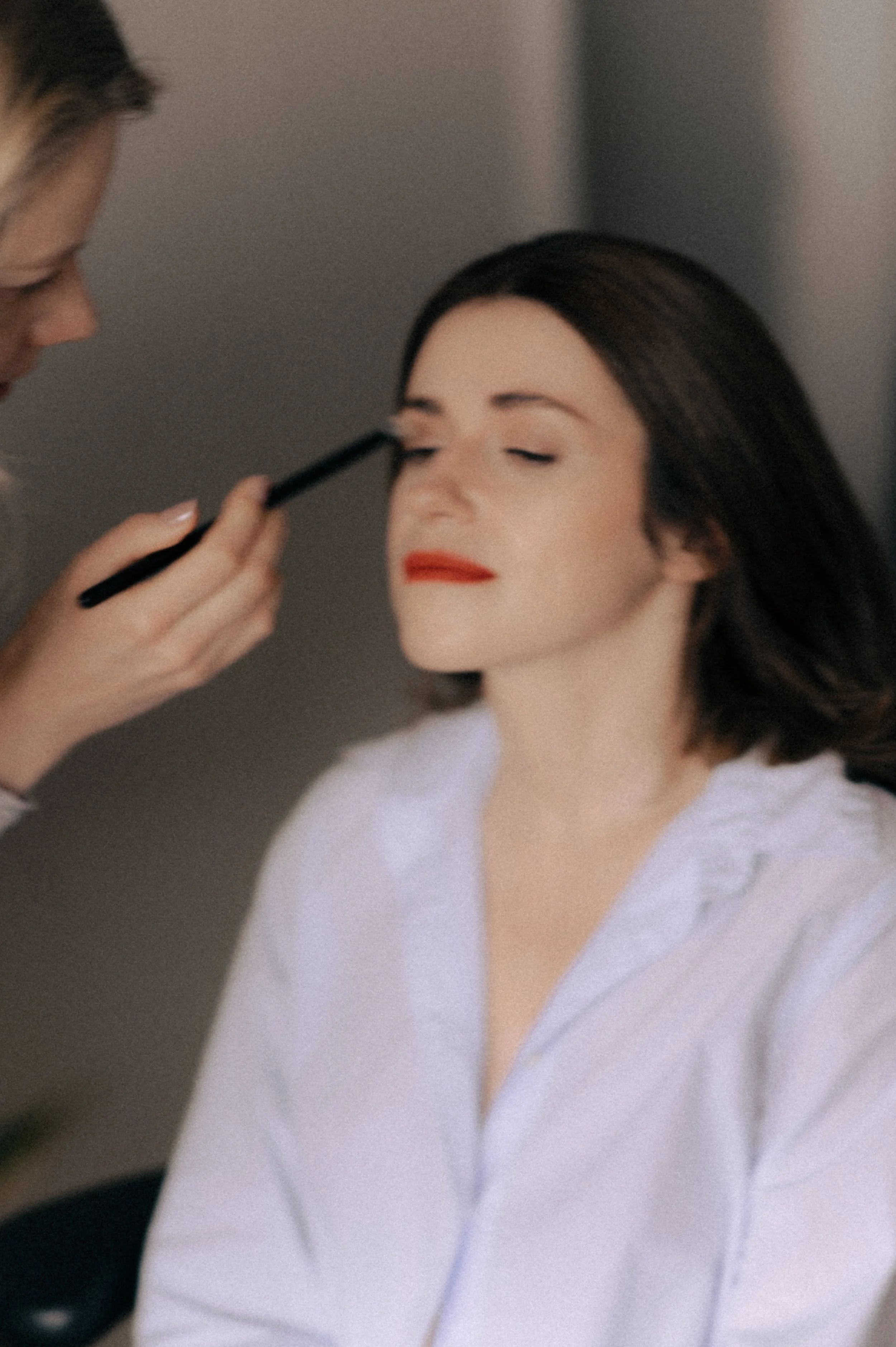 Woman with closed eyes getting makeup applied by a makeup artist.