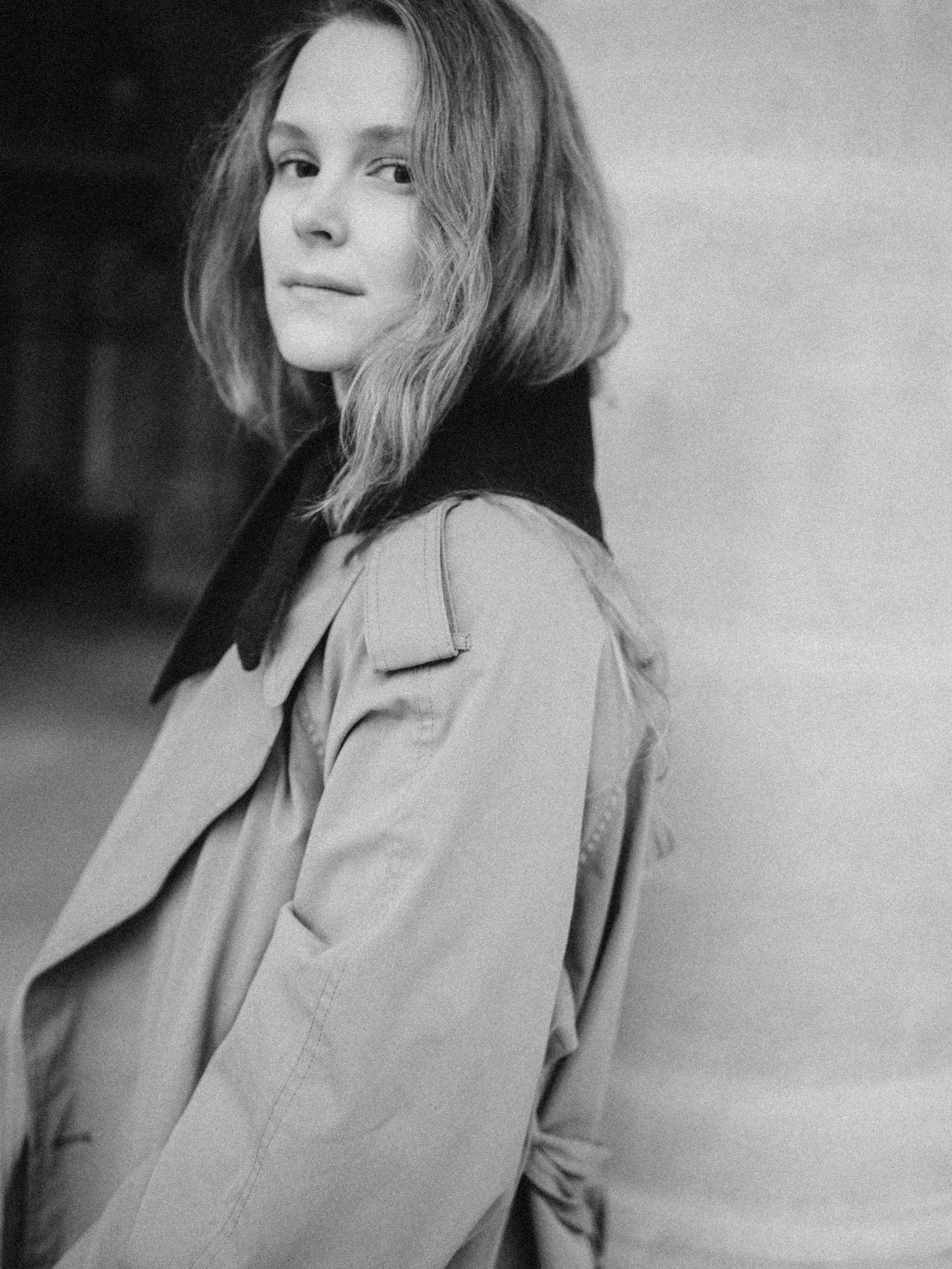Black and white photo of a woman with wavy hair wearing a trench coat with a dark collar.