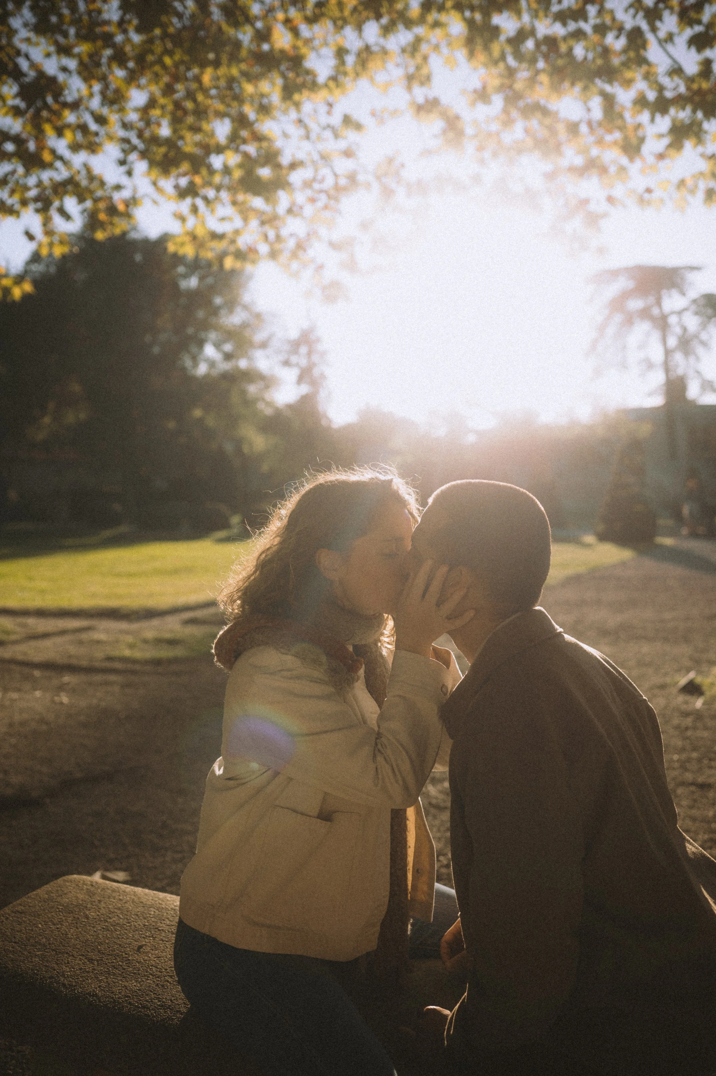 A couple sharing a kiss outdoors during sunset with trees in the background.