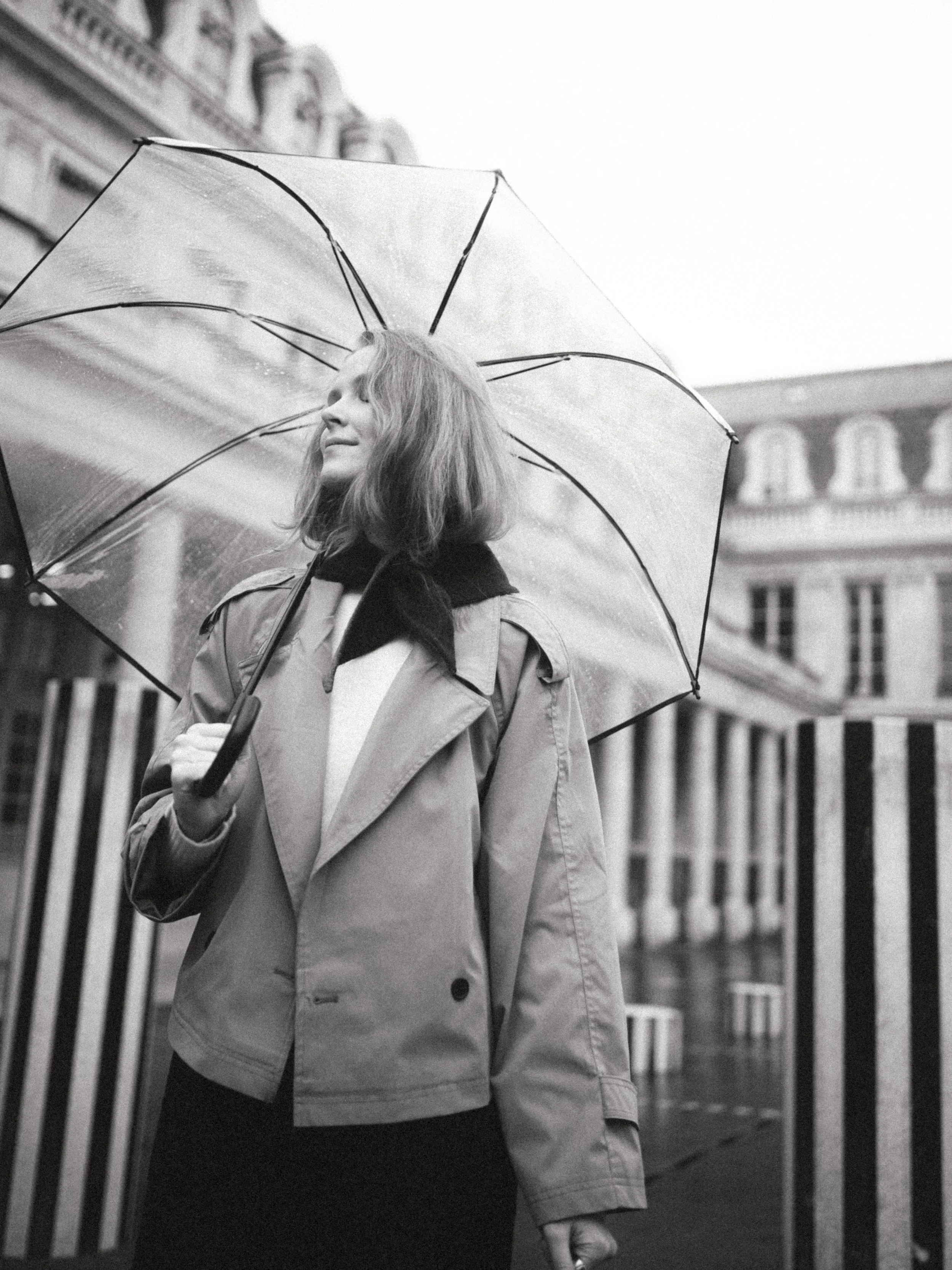 A woman holding an umbrella on a rainy day in an urban setting, smiling and looking to her left.