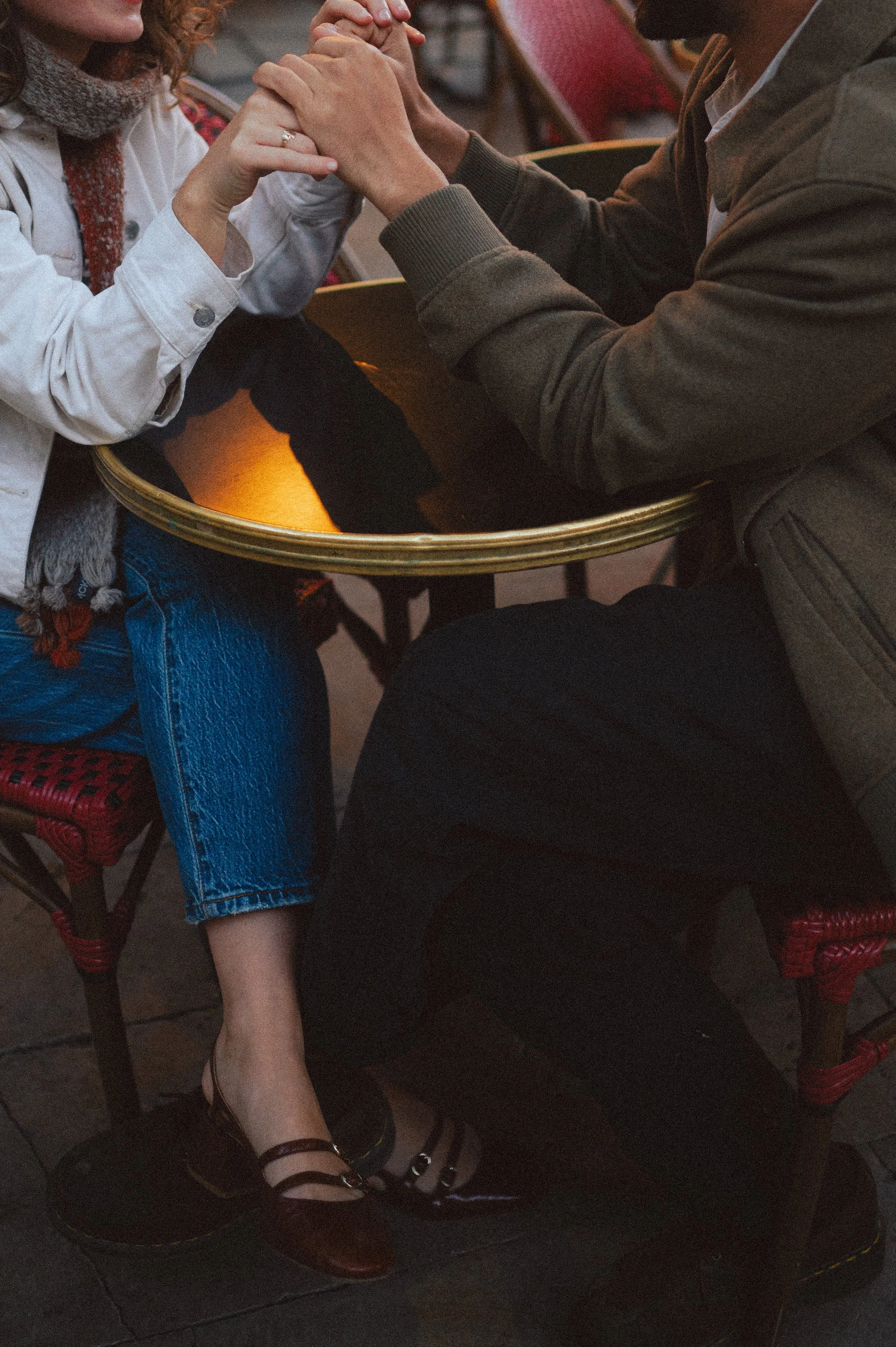 A couple holding hands across a small round table at an outdoor café.