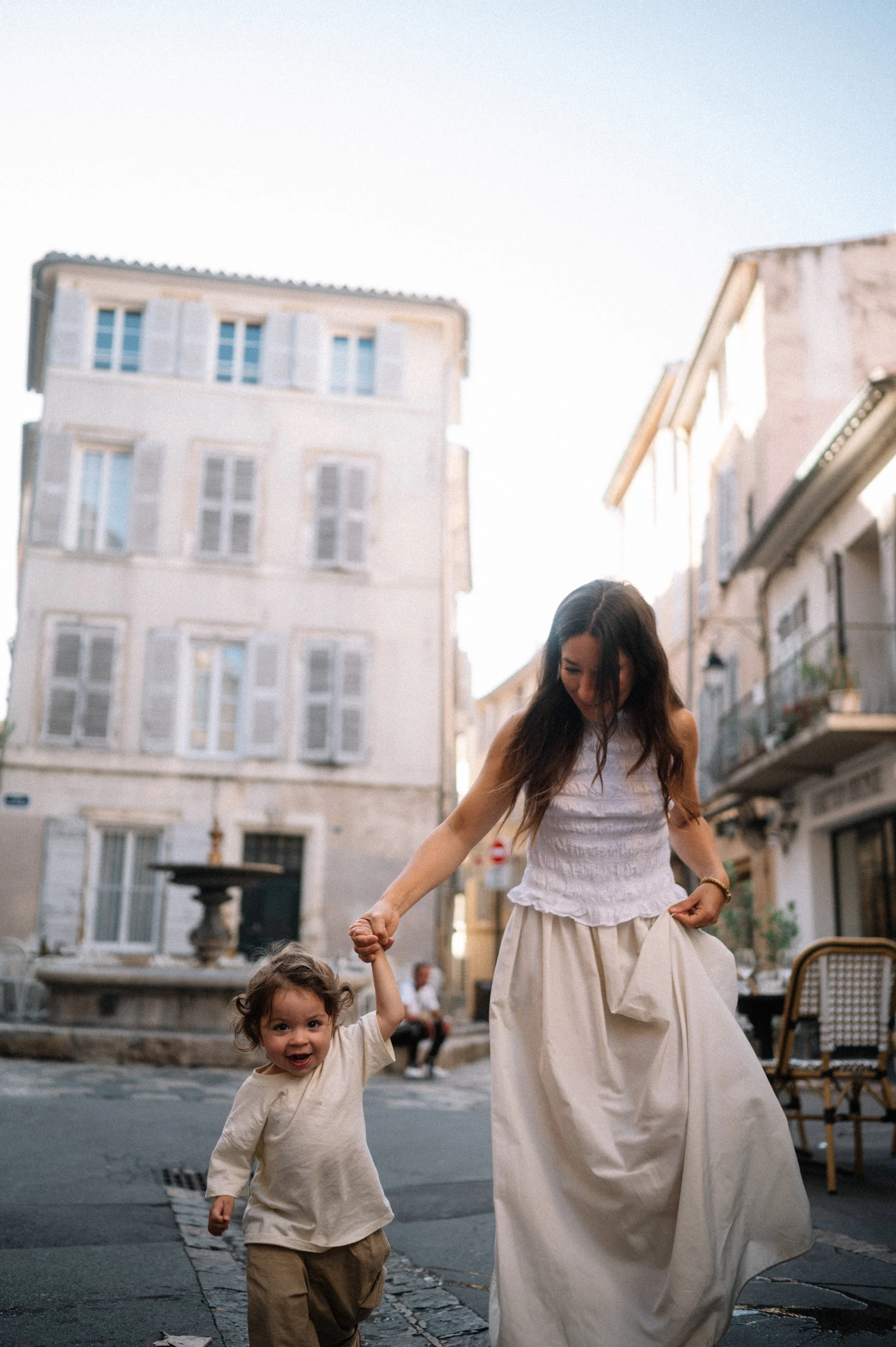 A woman and a young girl holding hands and playing on a street in a European city.