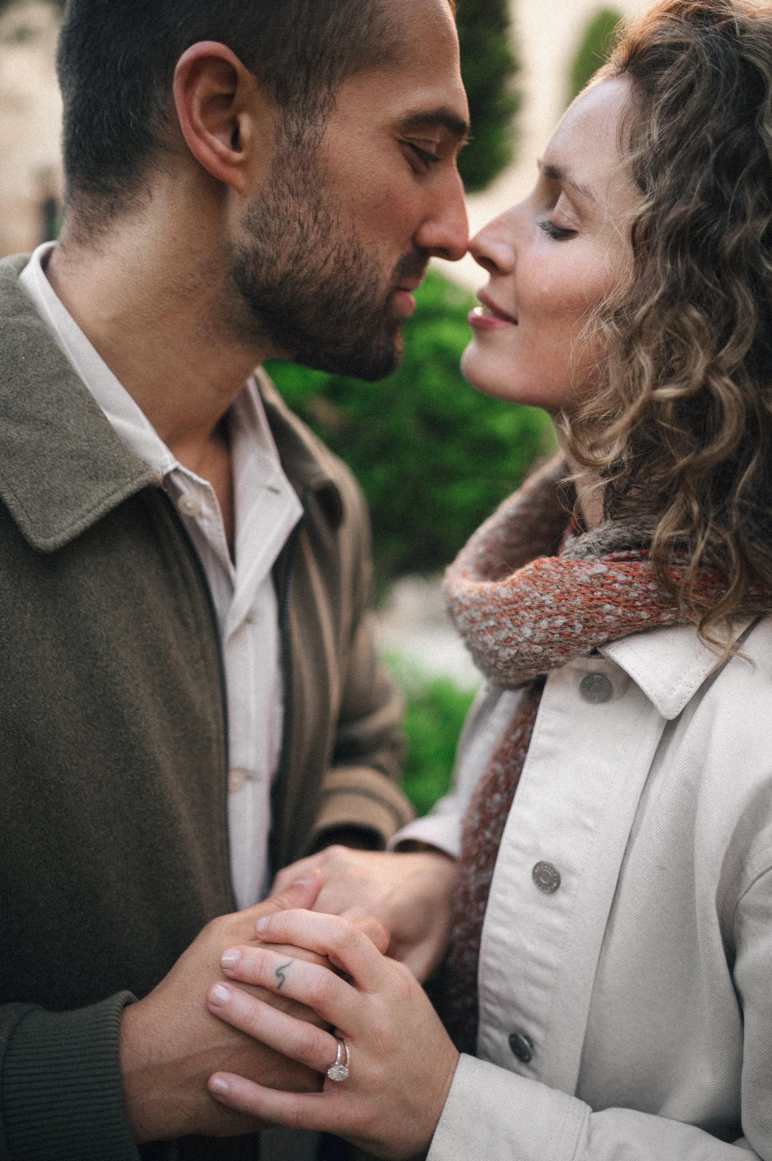 A couple is close together, about to kiss, holding hands with a ring visible on the woman's finger.