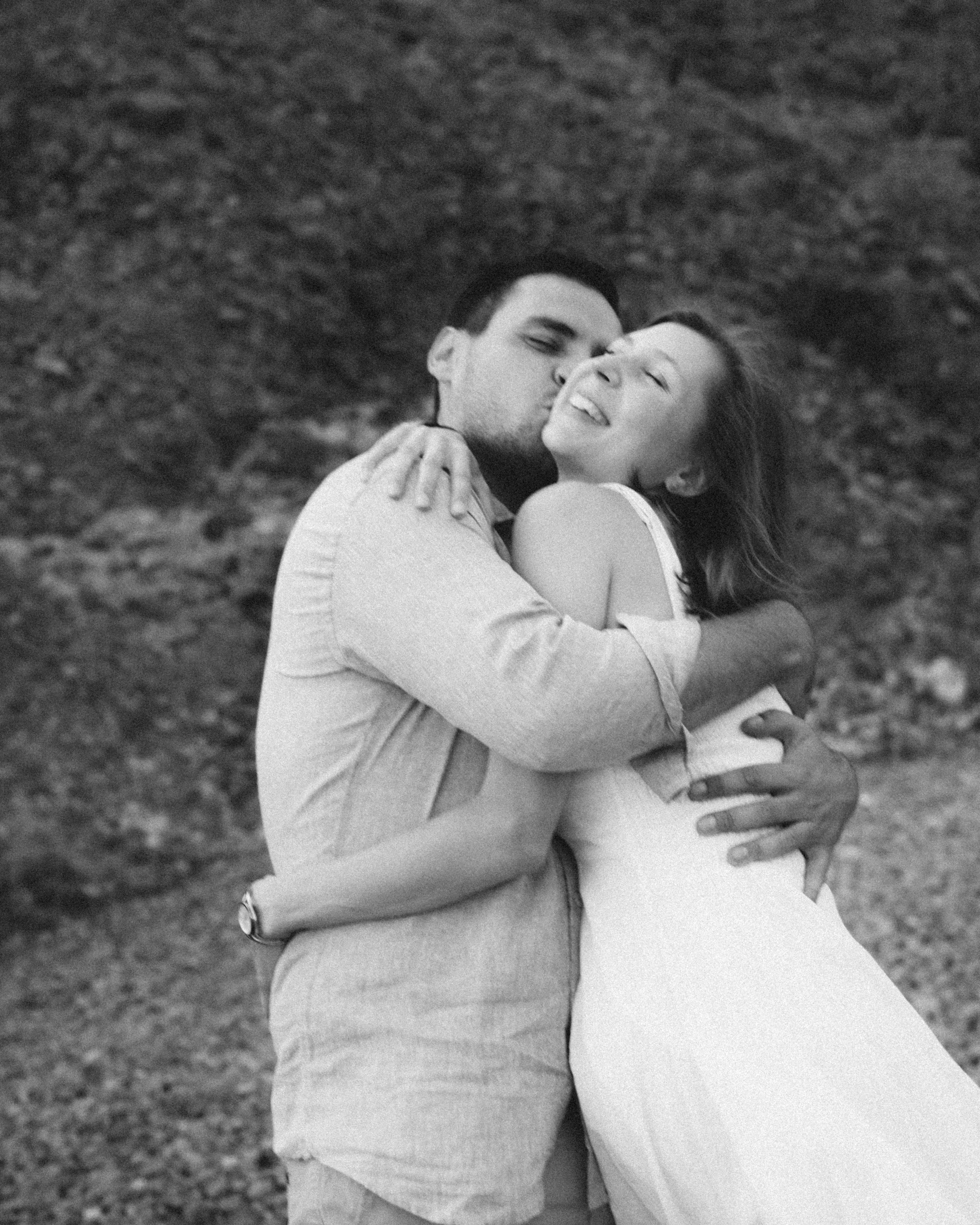 A black-and-white photo of a couple hugging and smiling outdoors.
