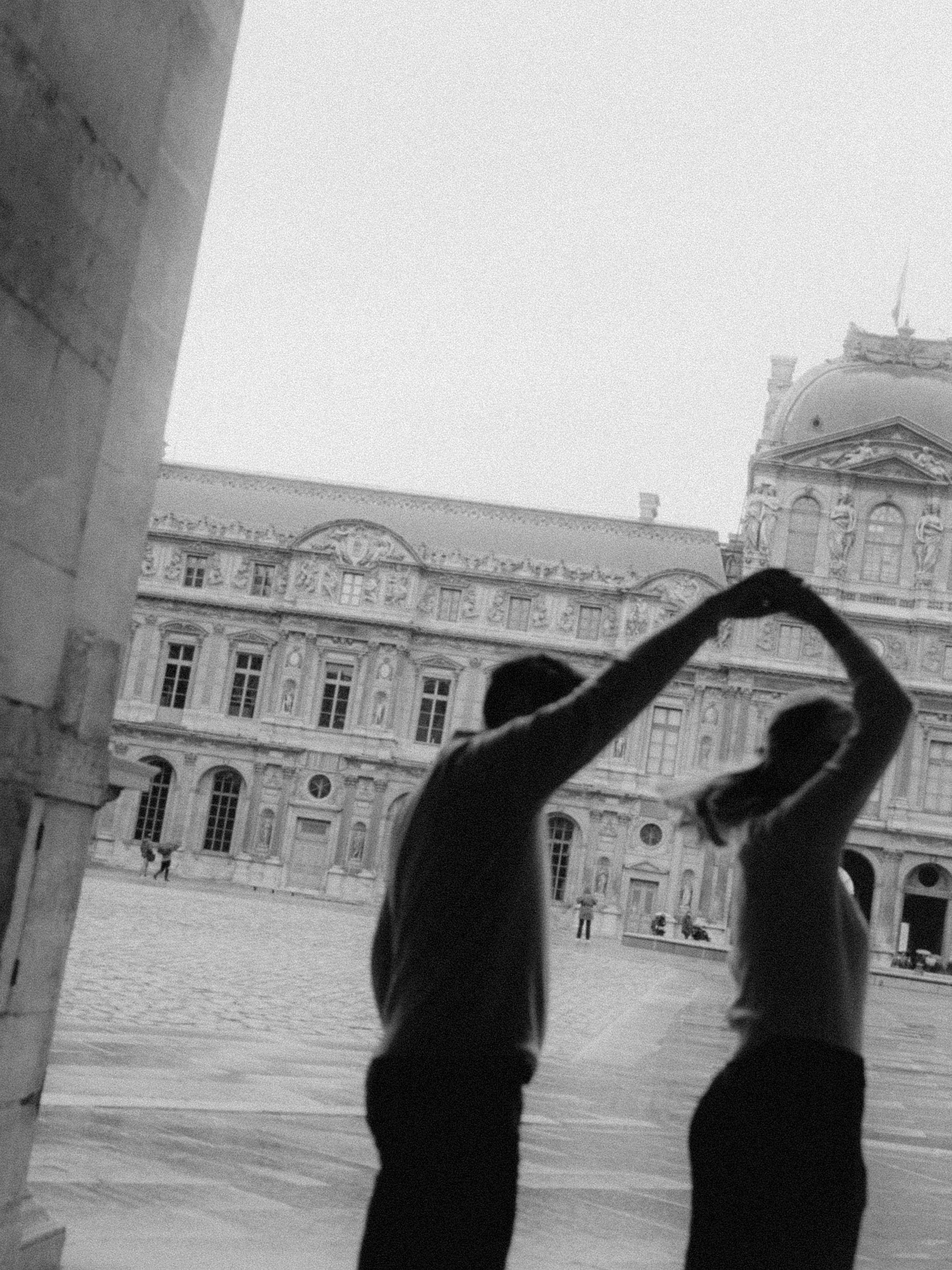 Silhouettes of a man and a woman holding hands in a dance pose in a courtyard with a historic building in the background.