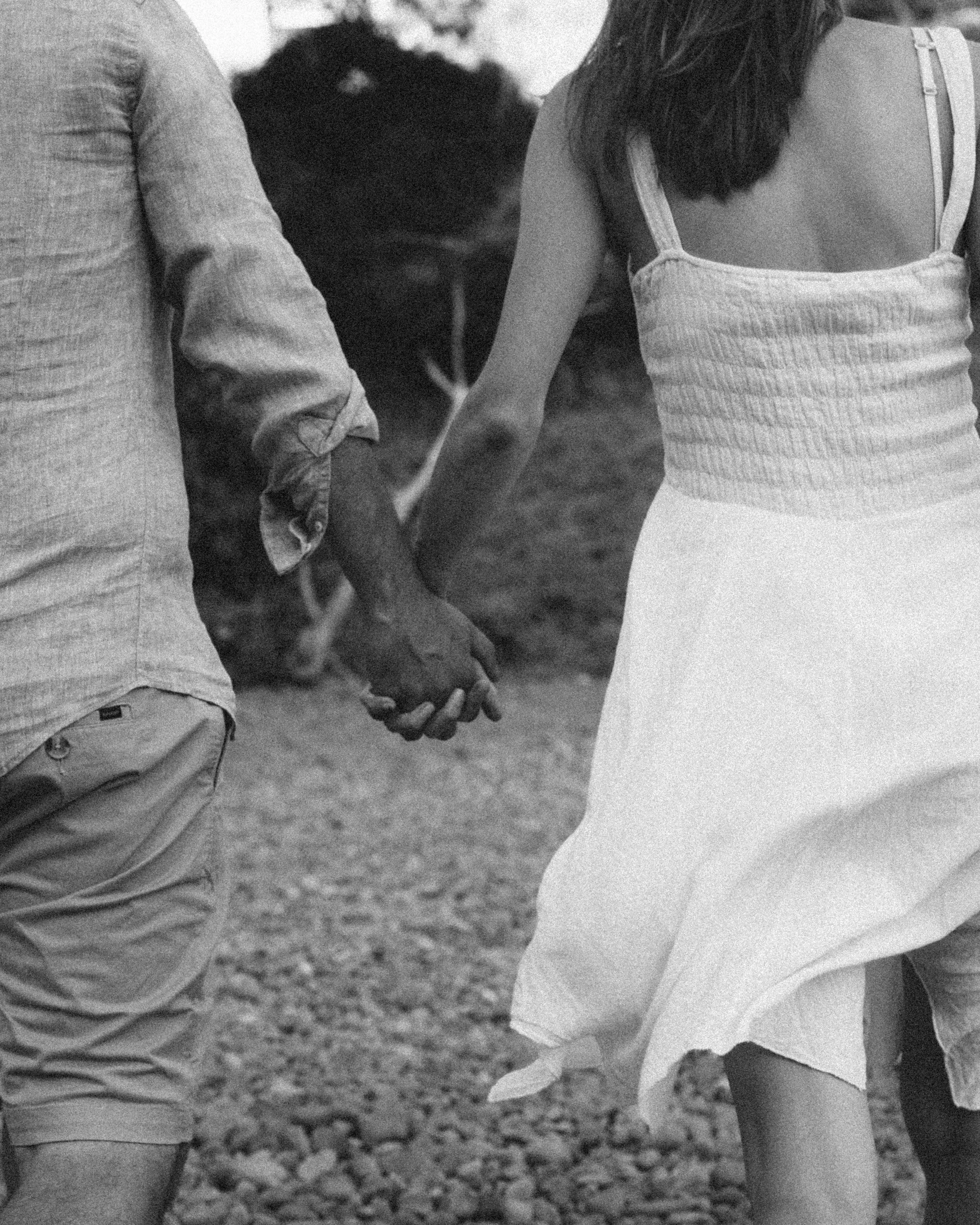A black and white photo of a man and a woman holding hands while walking outdoors.
