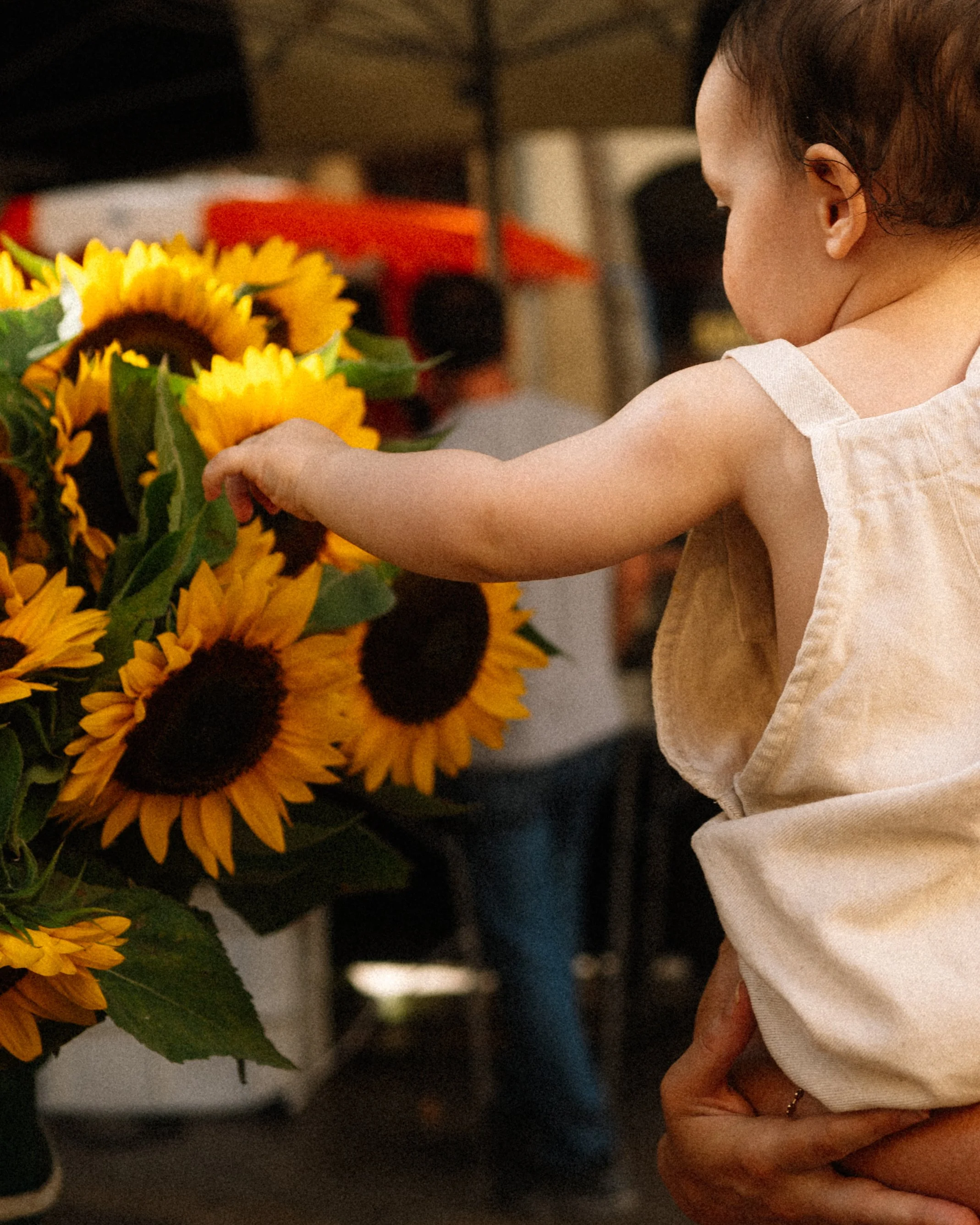 A young girl touching a bouquet of sunflowers in a market or shop.