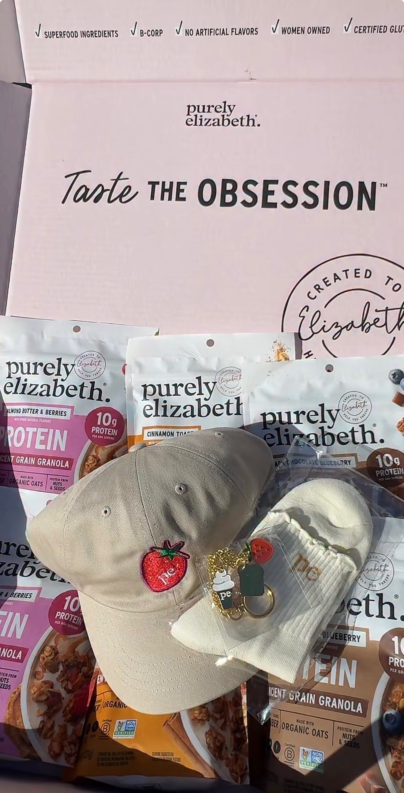A collection of Purely Elizabeth snack products, hats, and accessories display in front of a pink sign promoting the brand's qualities.