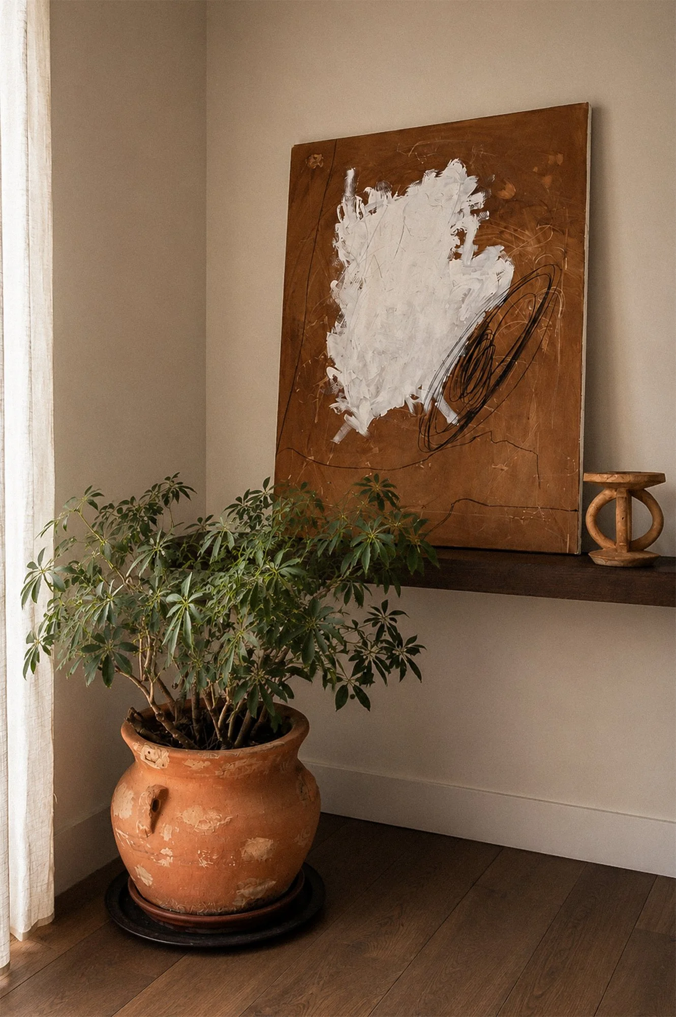 A kitchen with a large potted plant on a wooden floor, a wall-mounted shelf with an abstract art piece, and a wooden sculpture on the shelf.