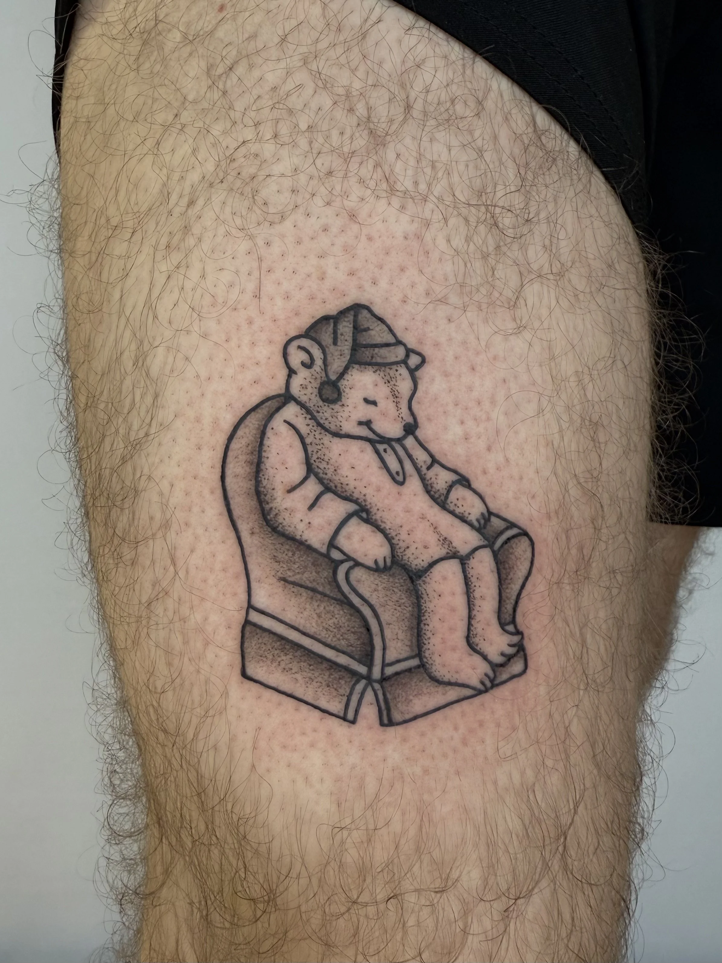 Tatouage d'un ours assis dans un fauteuil en train de dormir, portant un bonnet et tenant une canne.