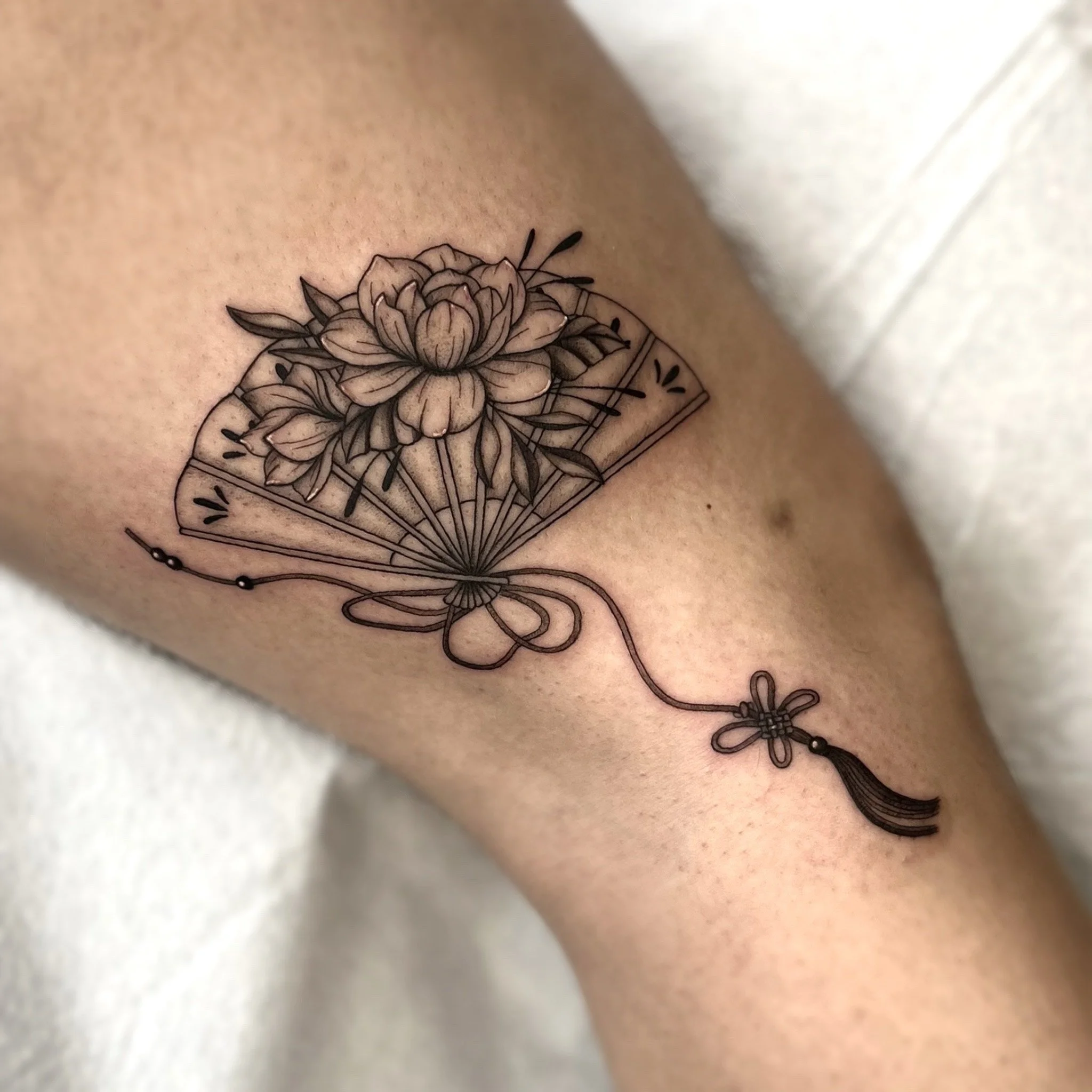 Tatouage d'un éventail stylisé avec une grande fleur au centre et une plume suspendue.