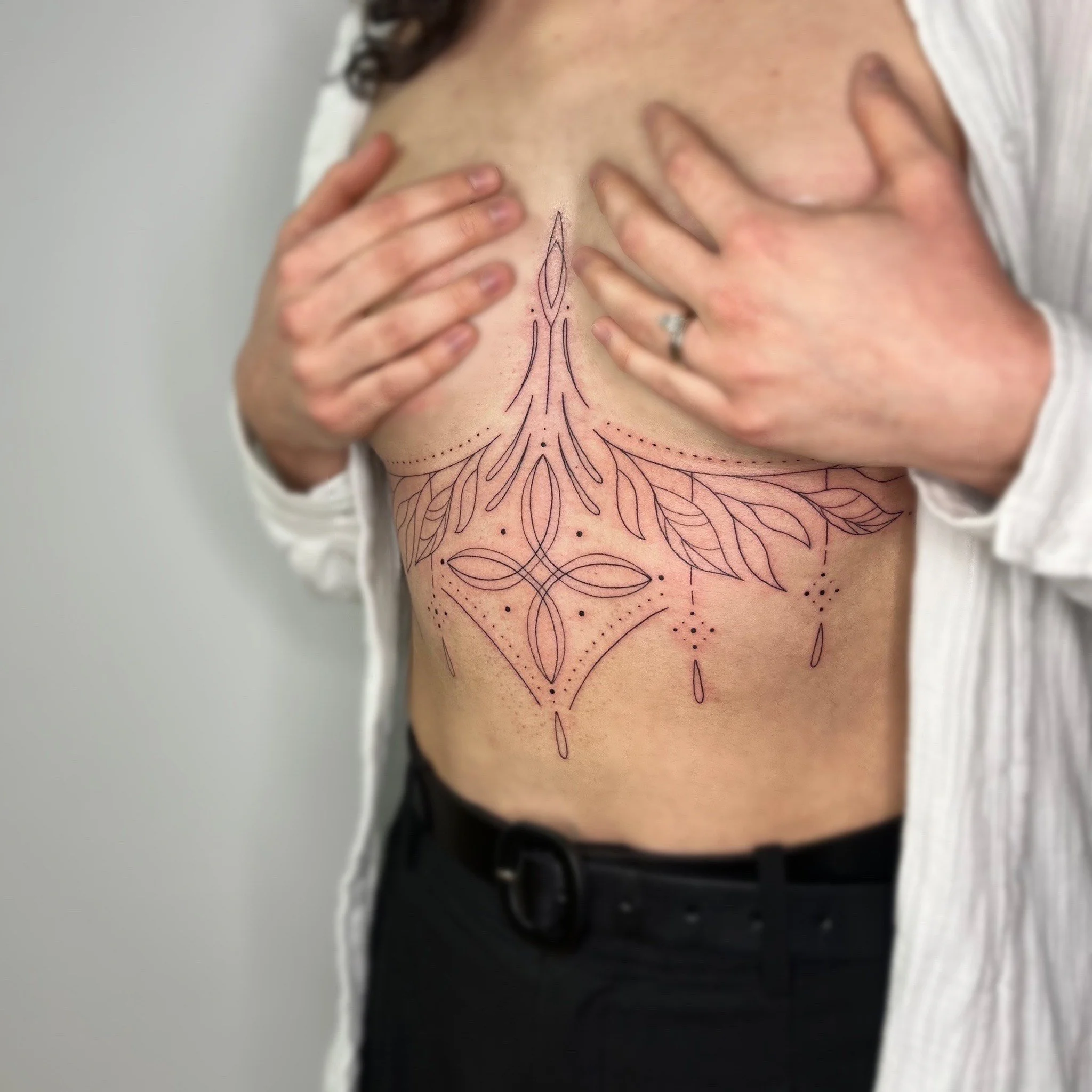 Une personne montrant une nouvelle tatouage sur le côté de la poitrine. Le tatouage consiste en un dessin de lignes délicates et motifs floraux.