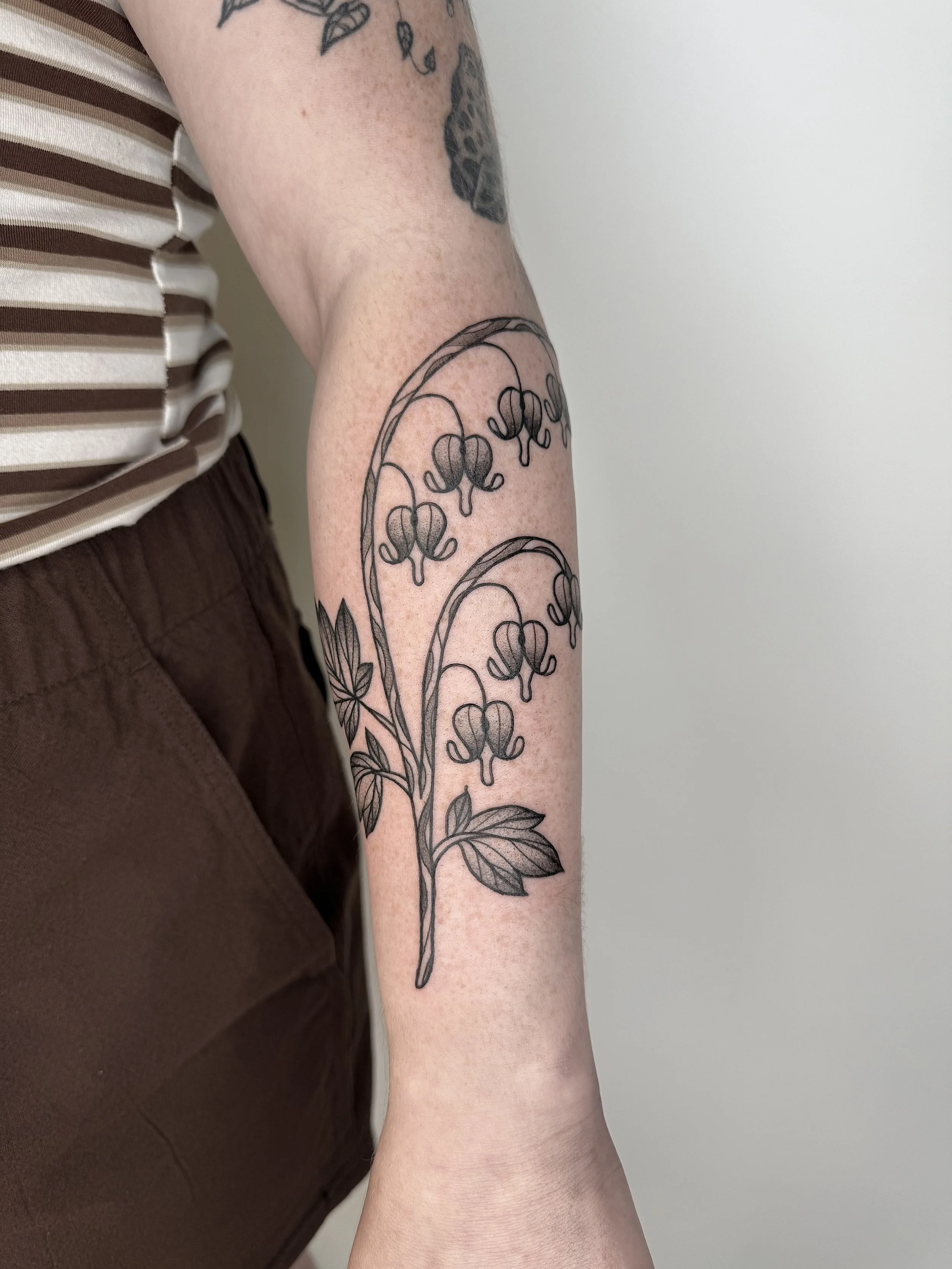 Tatouage d'une branche avec des fleurs en haut du bras.