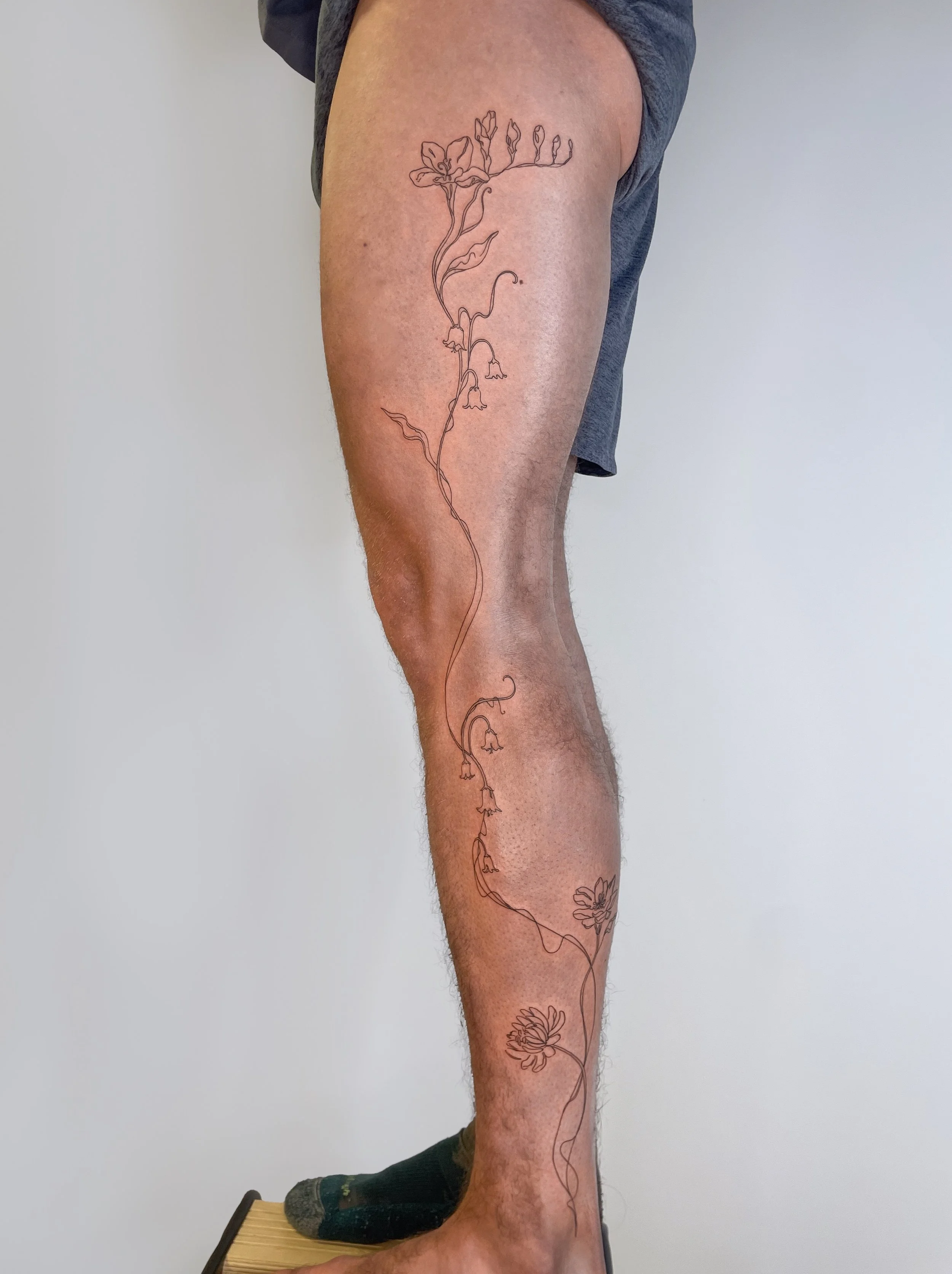 Tatouage d'une plante ou d'une fleur délicate en ligne sur la jambe d'un homme.