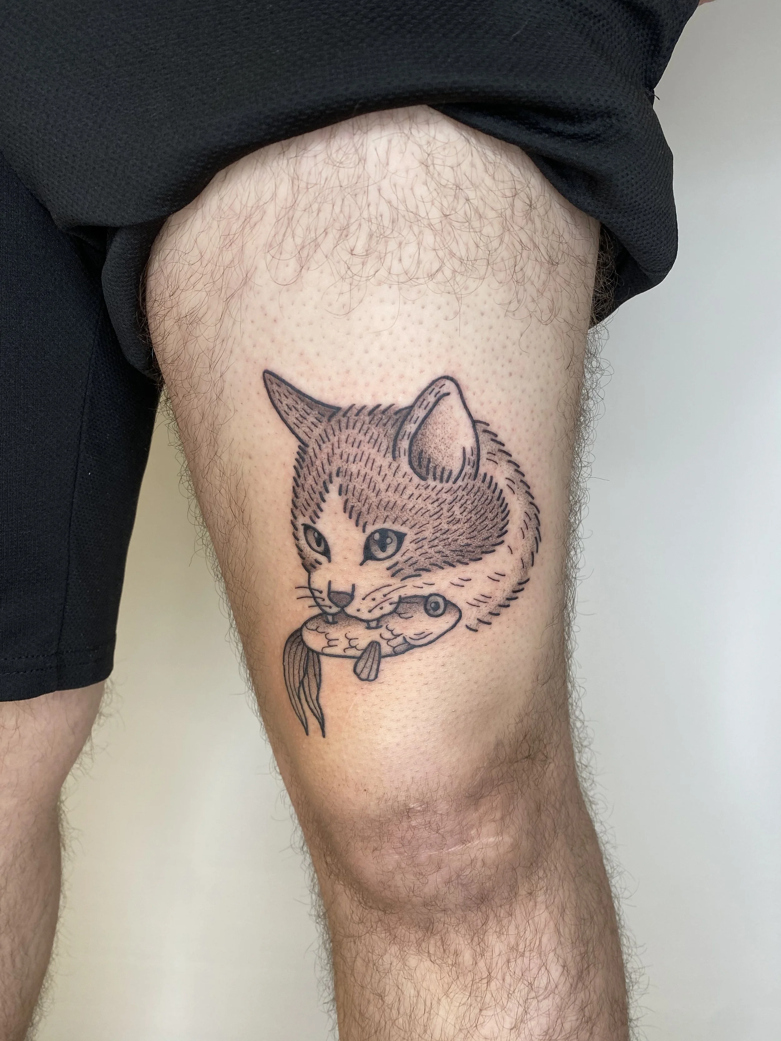 Tatouage d'un chat tenant un poisson dans la jambe d'une personne.