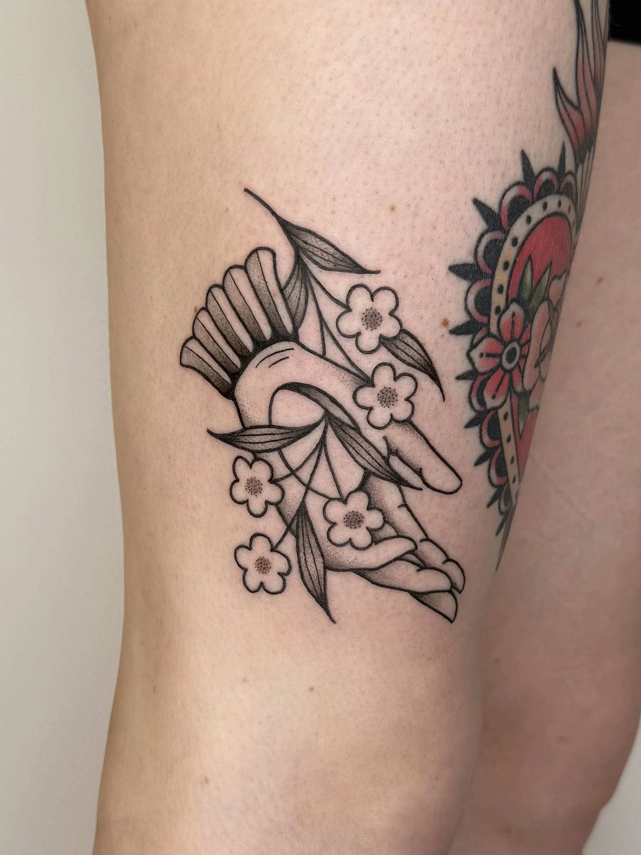 Tatouage d'un oiseau avec des fleurs et des feuilles en noir et blanc sur la peau.