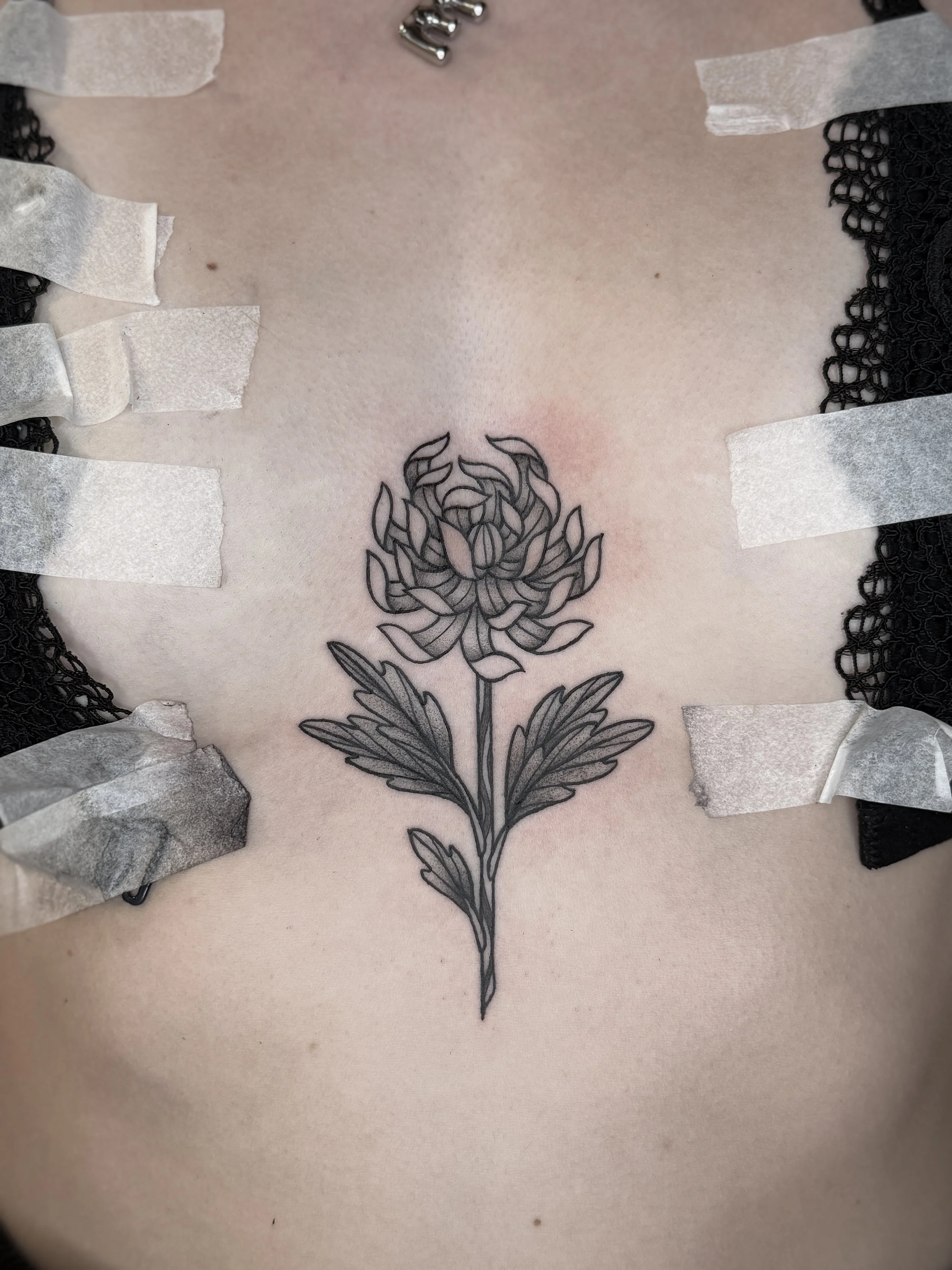 Tatouage d'une fleur, probablement une chrysanthème, sur la poitrine d'une personne, entouré de rubans et de bandages