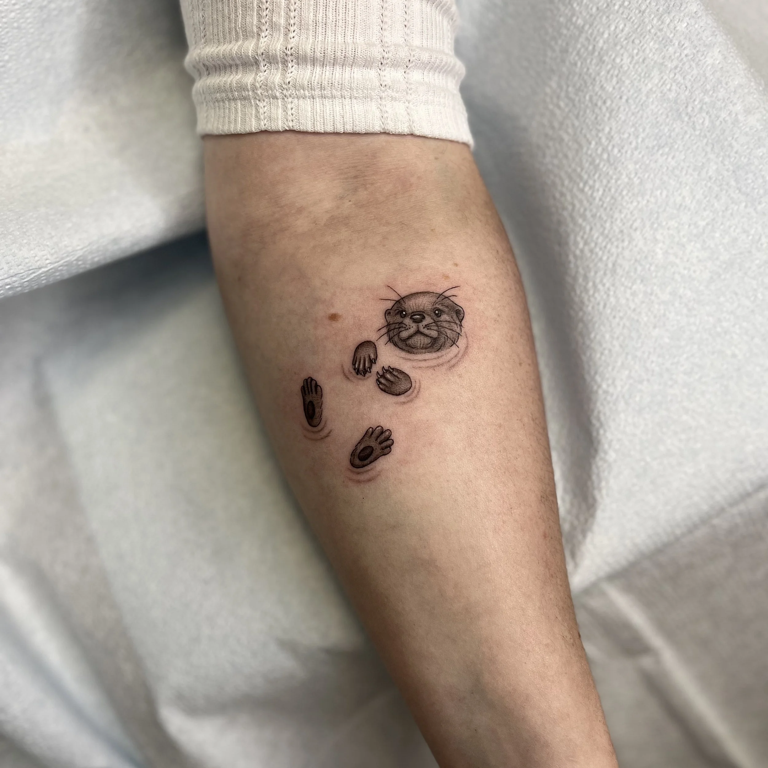Tatouage d'une loutre avec des motifs de mains de différentes tailles sur le bras