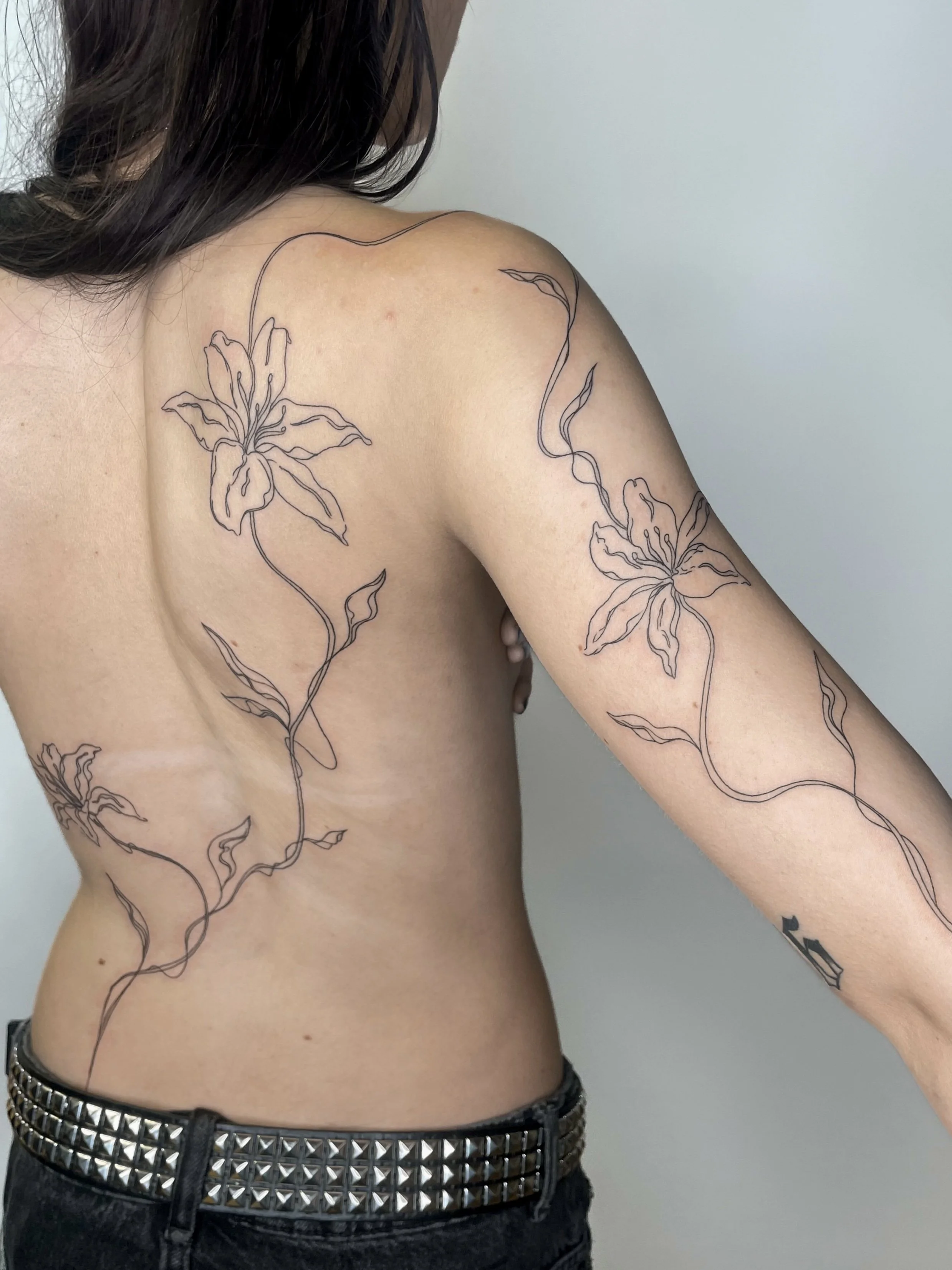 Tatouages de fleurs et de feuilles en lignes noires sur l'épaule, le bras et le côté.