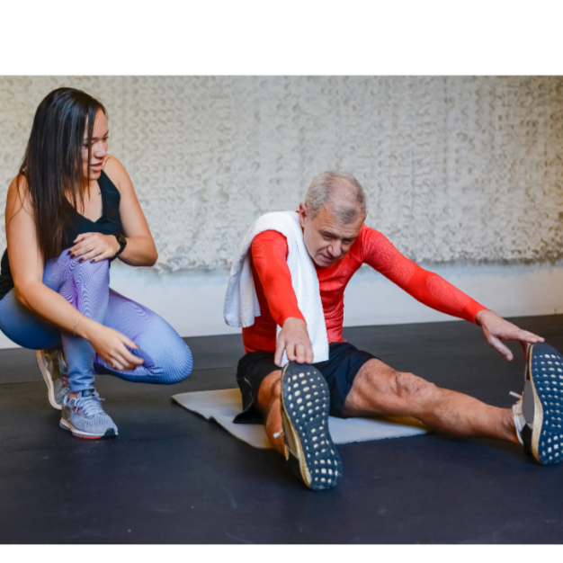 A woman in black shirt assisting a man in an orange shirt while he stretches.