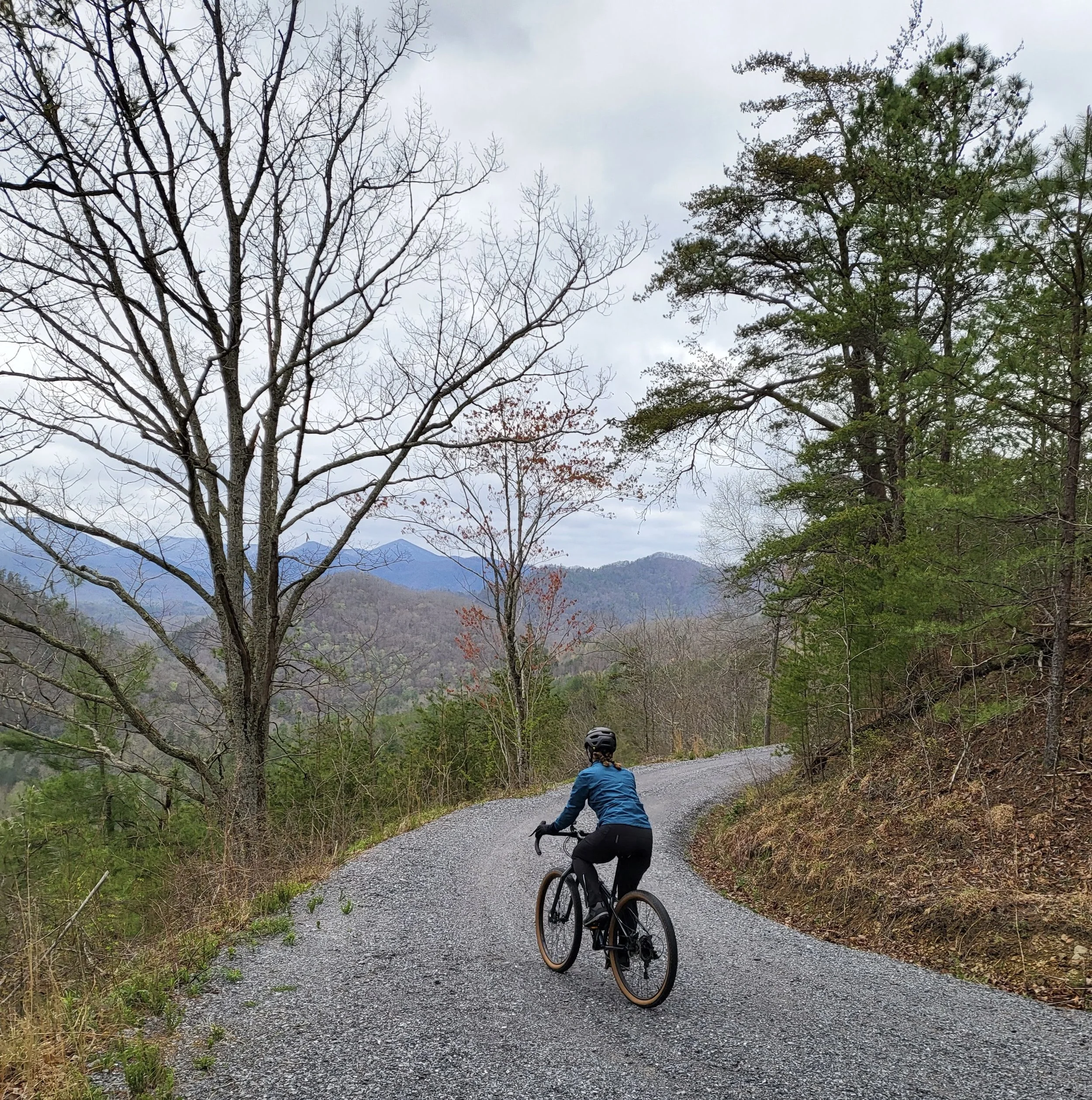 A cyclist riding along a quiet gravel road through the mountains, reflecting movement and forward momentum.