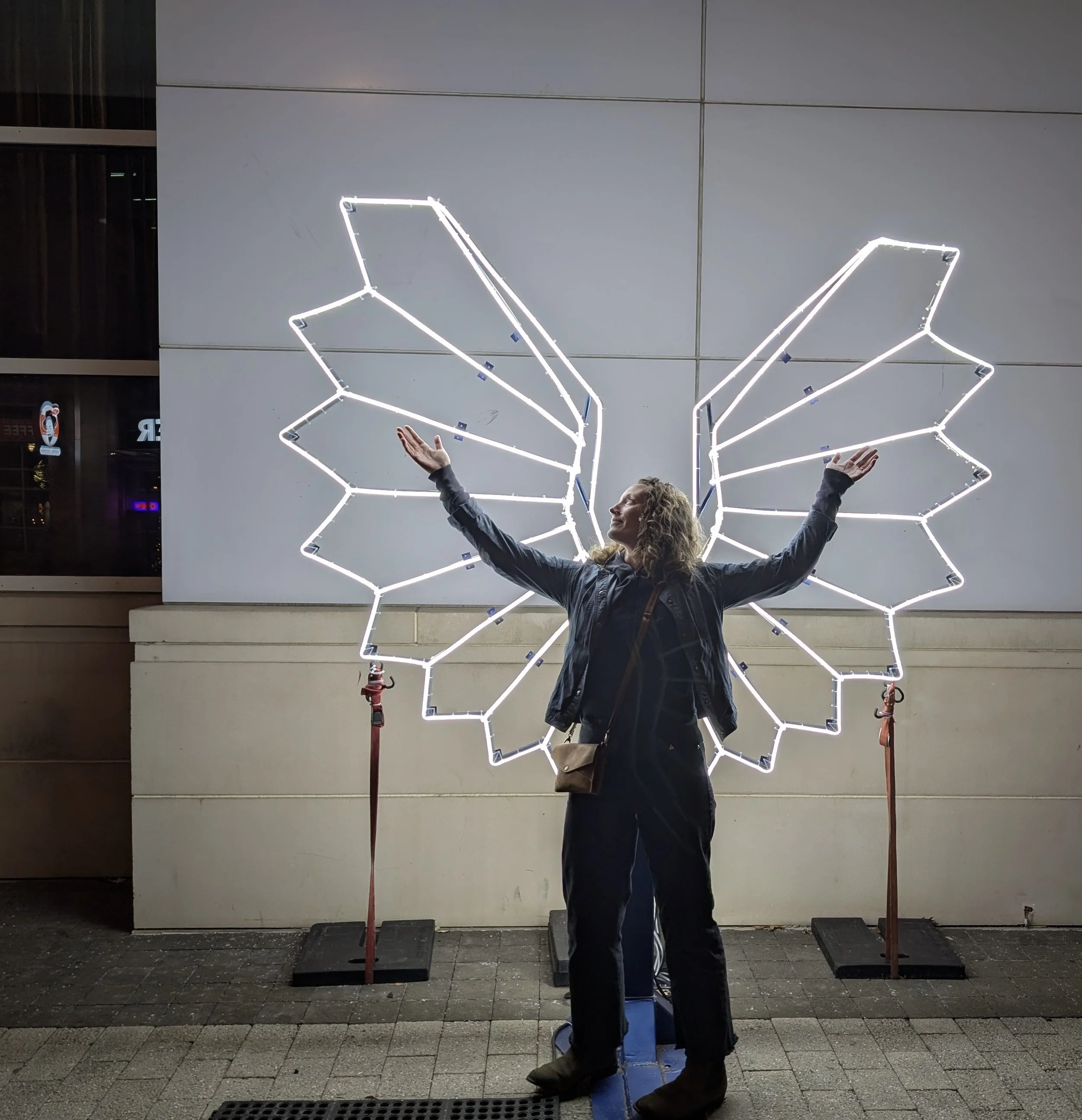 A woman standing with illuminated wings behind her, symbolizing self-expression, courage, and personal growth.