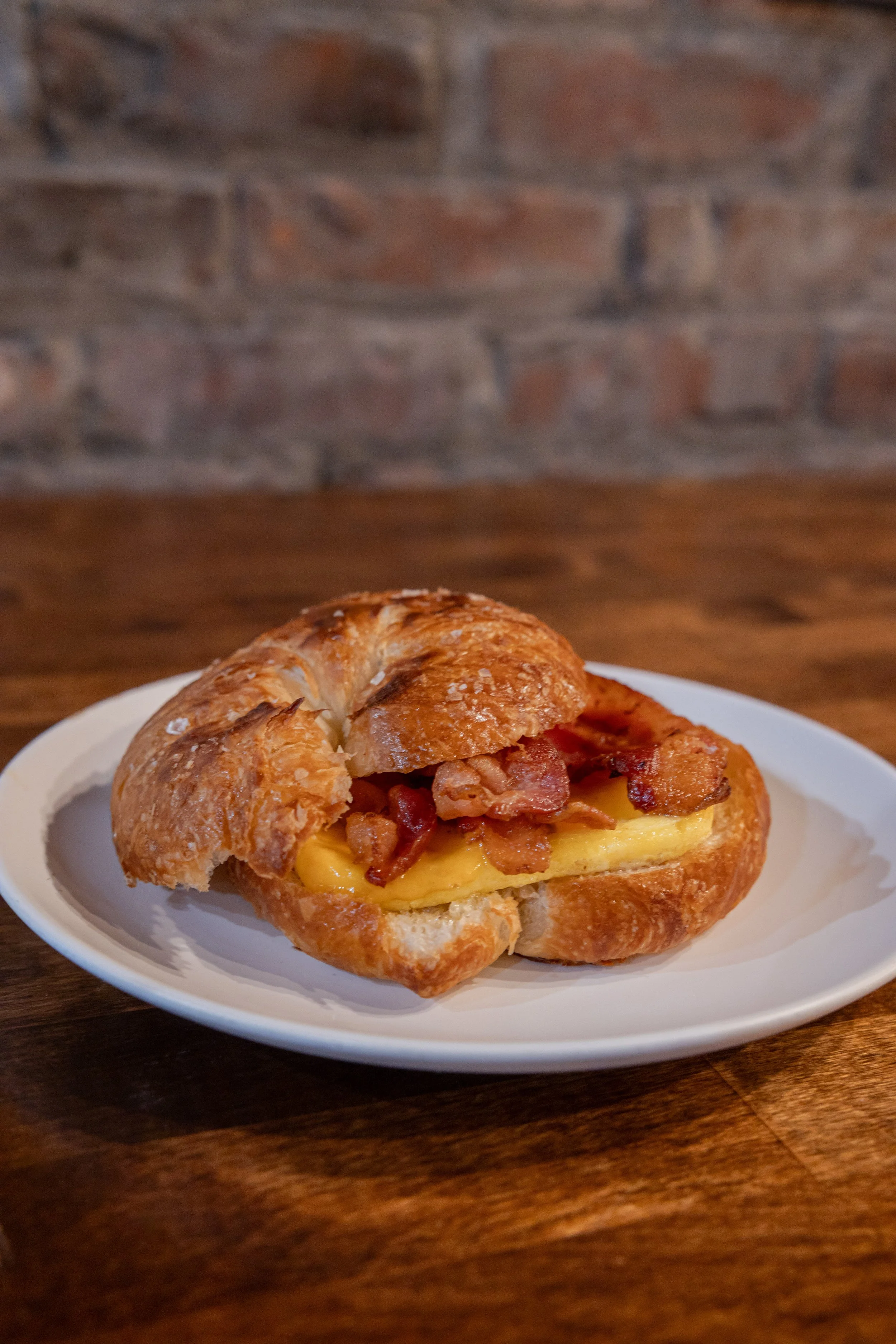 Bacon, cheese, and egg breakfast sandwich on a croissant, served on a white plate.