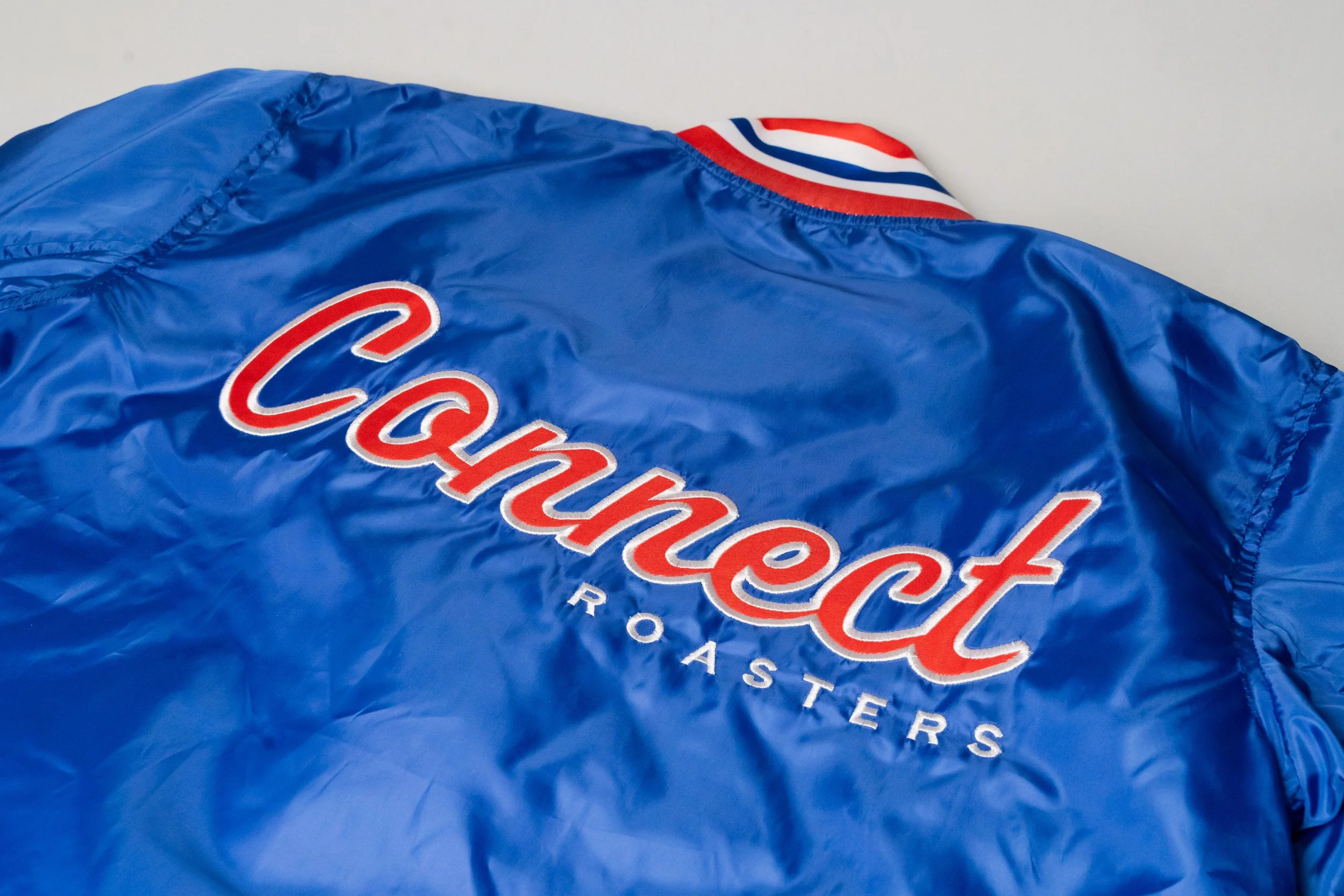 Blue satin jacket with Champion logo and 'Rosters' embroidered on the back, with red, white, and blue striped accents.