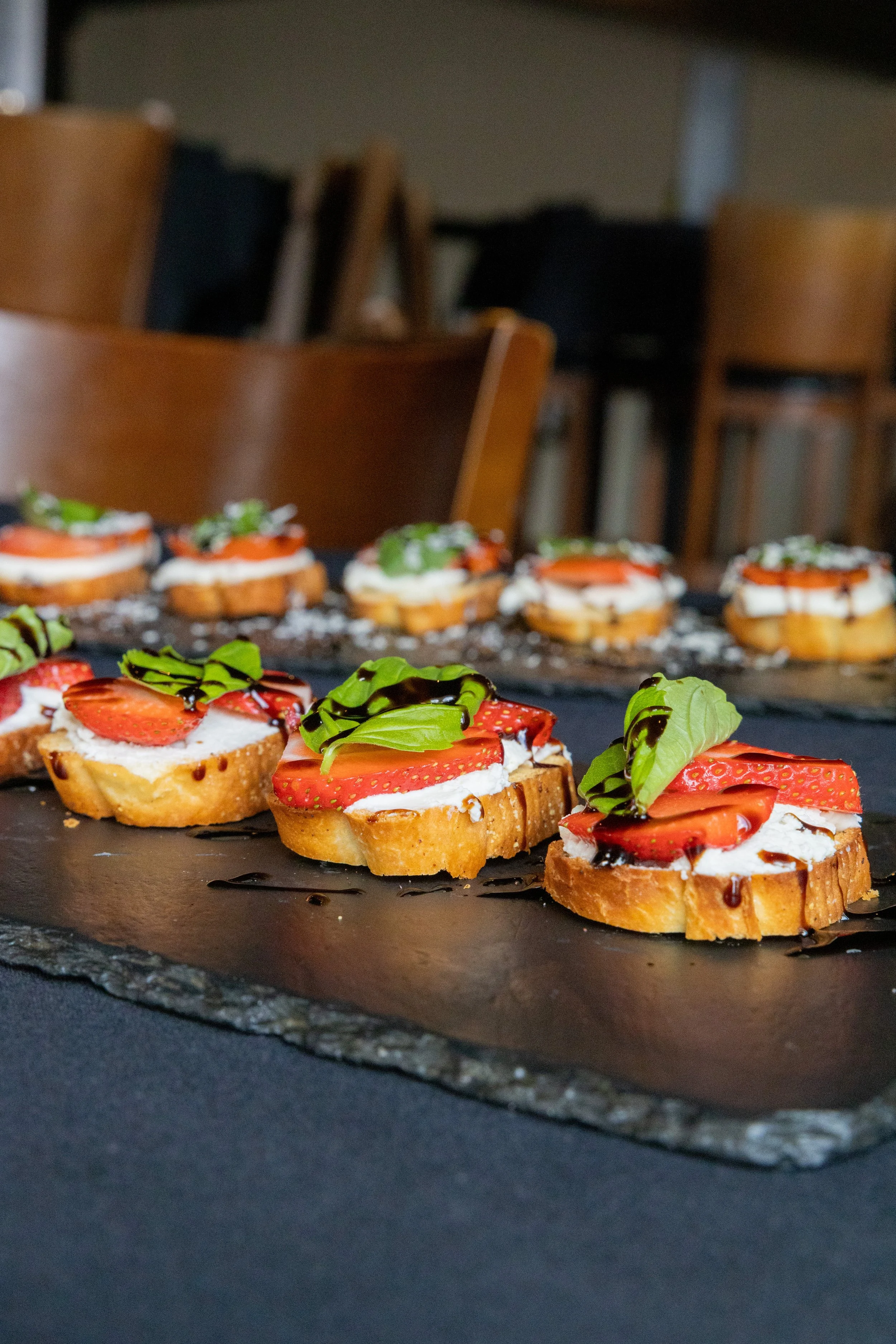 Close-up of strawberry and basil-topped crostinis drizzled with balsamic glaze on a slate serving platter.