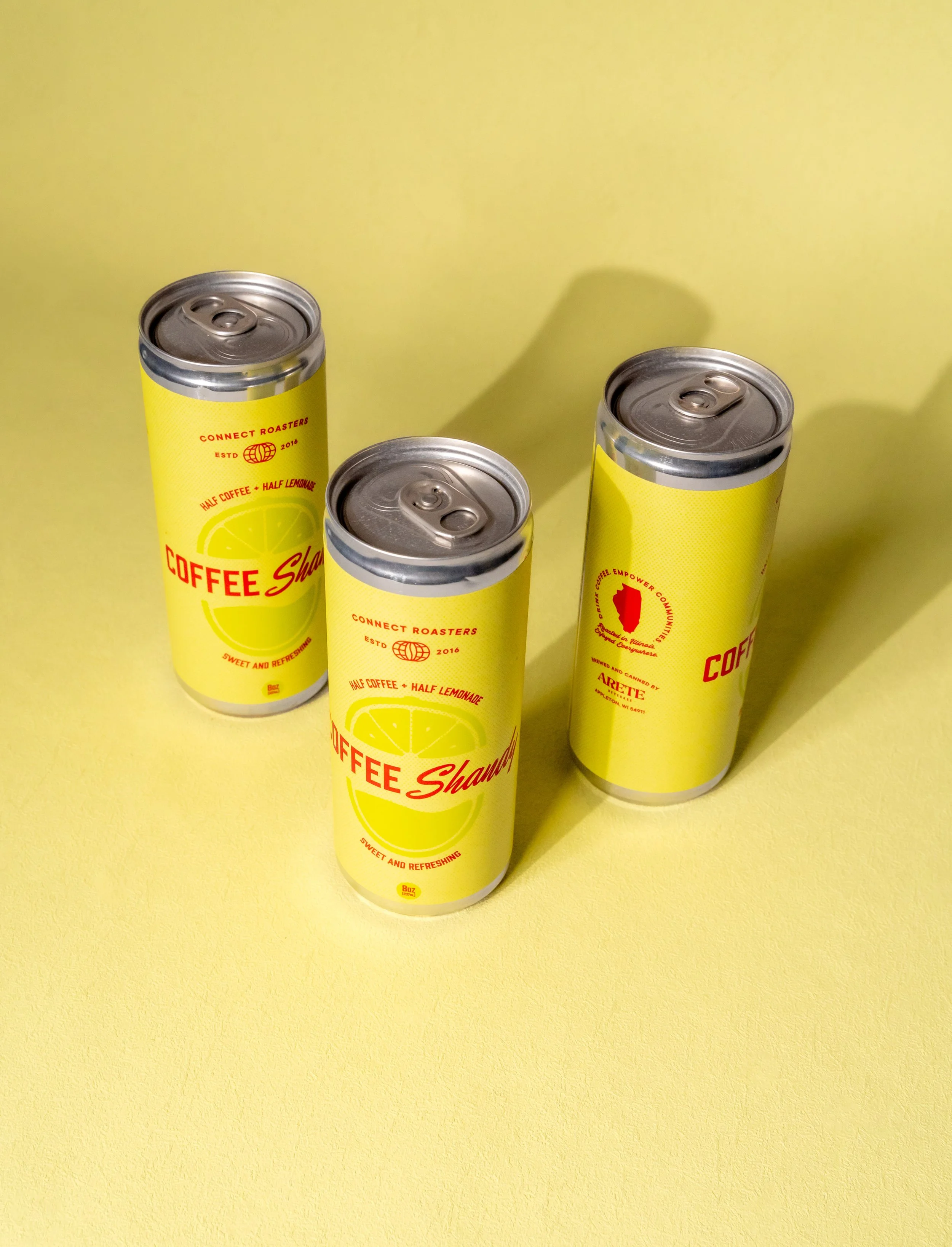 Three yellow cans with red and white text and lemon images, on a yellow background.