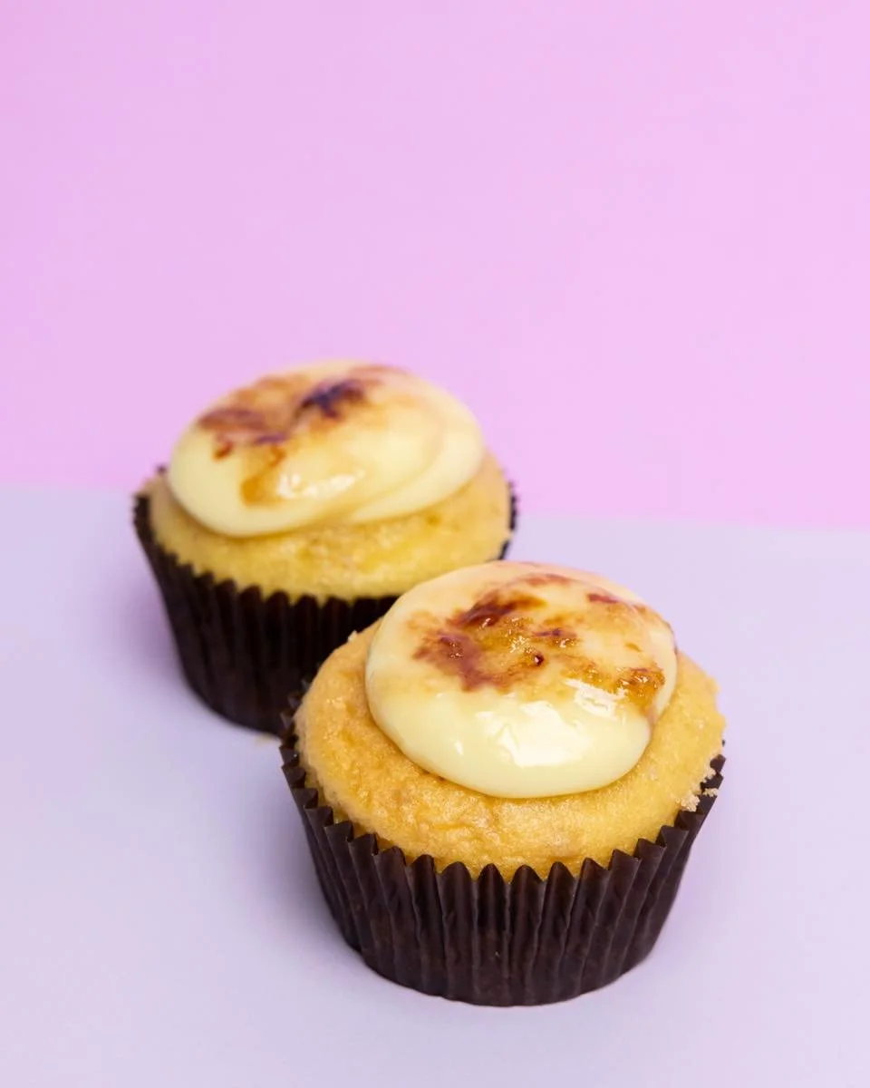 Two cupcakes with creamy icing topping on a pink and purple background.