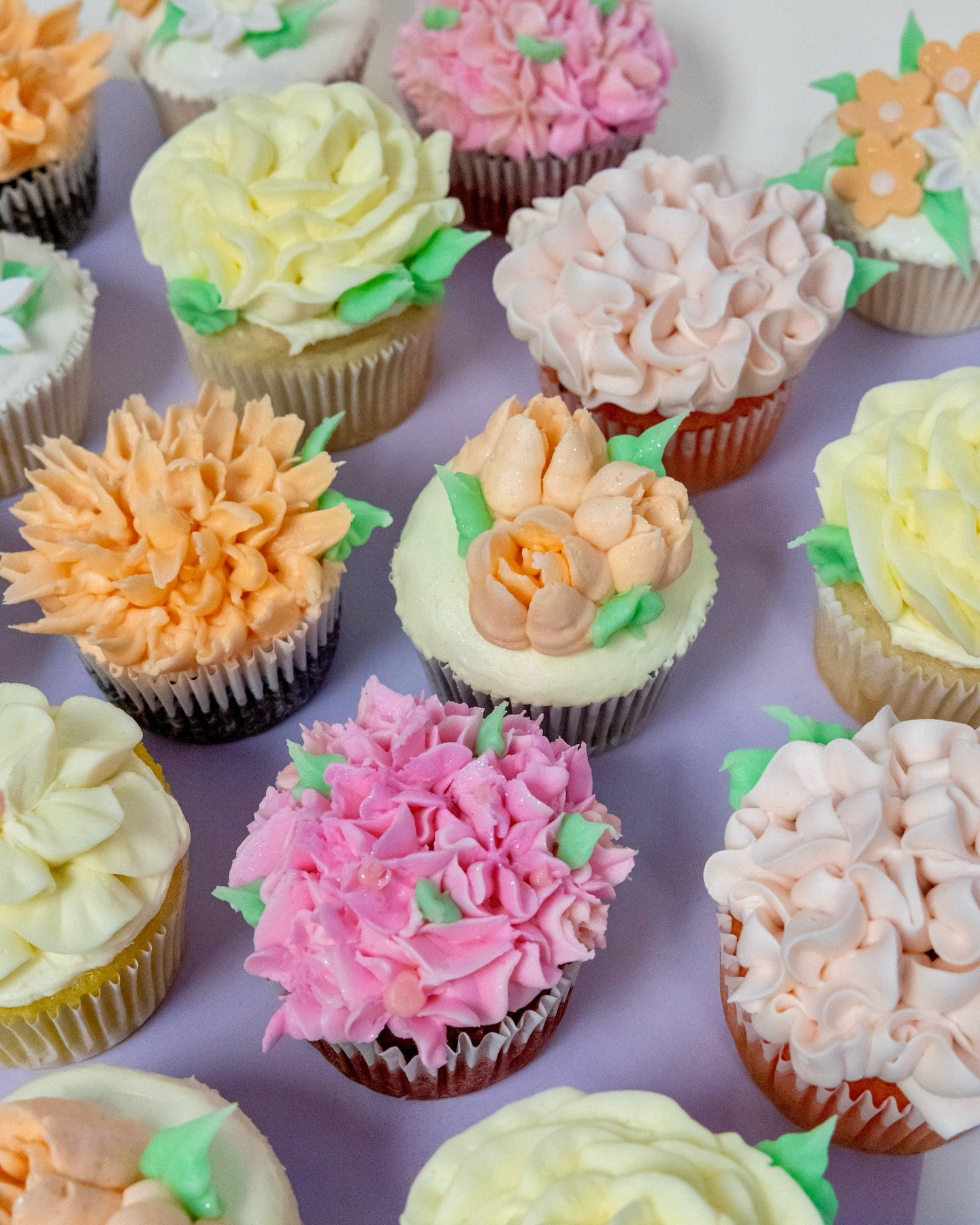 Assorted cupcakes decorated with pastel-colored frosting and floral designs.