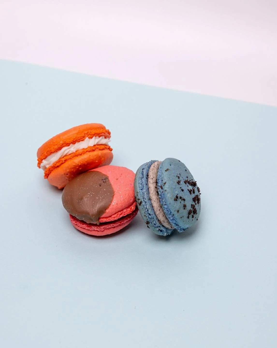 Three colorful macarons on a light blue surface with a white background.