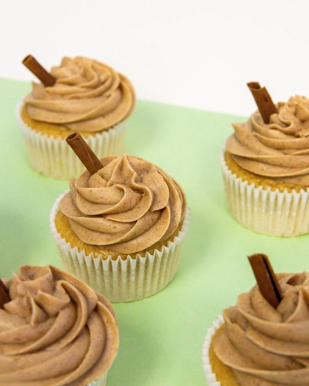 Cupcakes with cinnamon frosting topped with cinnamon sticks on a light green surface.