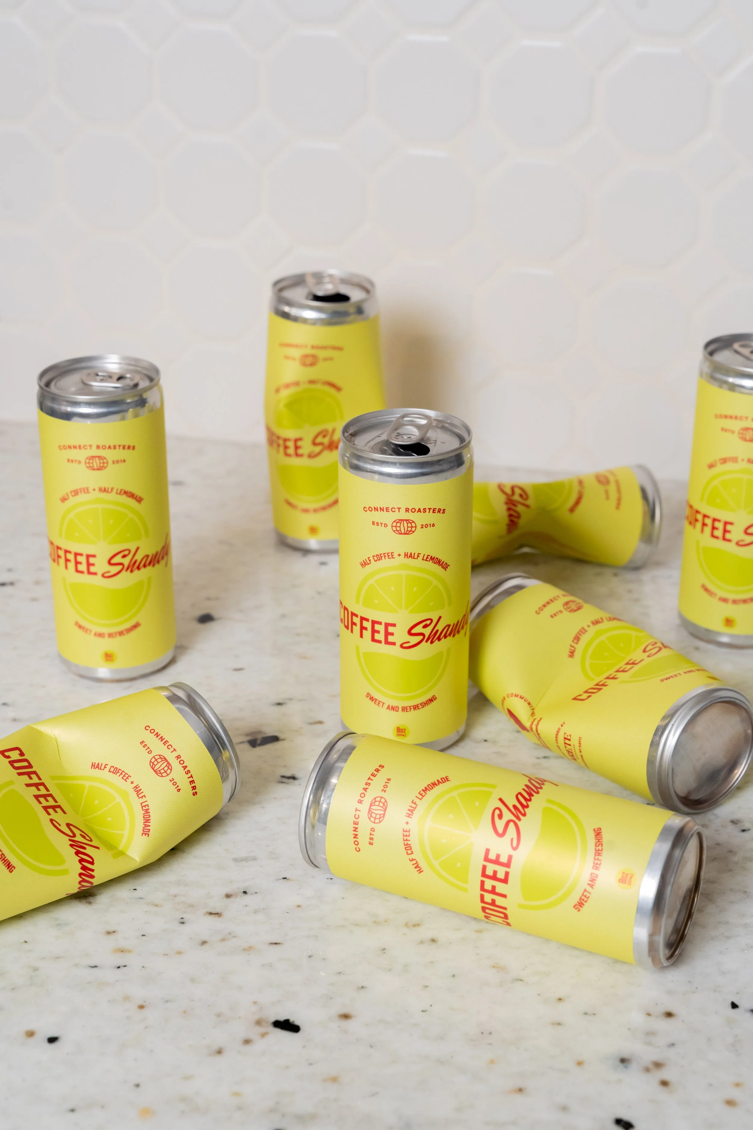 Multiple yellow cans of coffee-flavored beverage labeled 'Coffee Shawarma' with lemon slices and text such as 'half coffee, half lemonade' and 'sweet and refreshing' on a white speckled countertop.