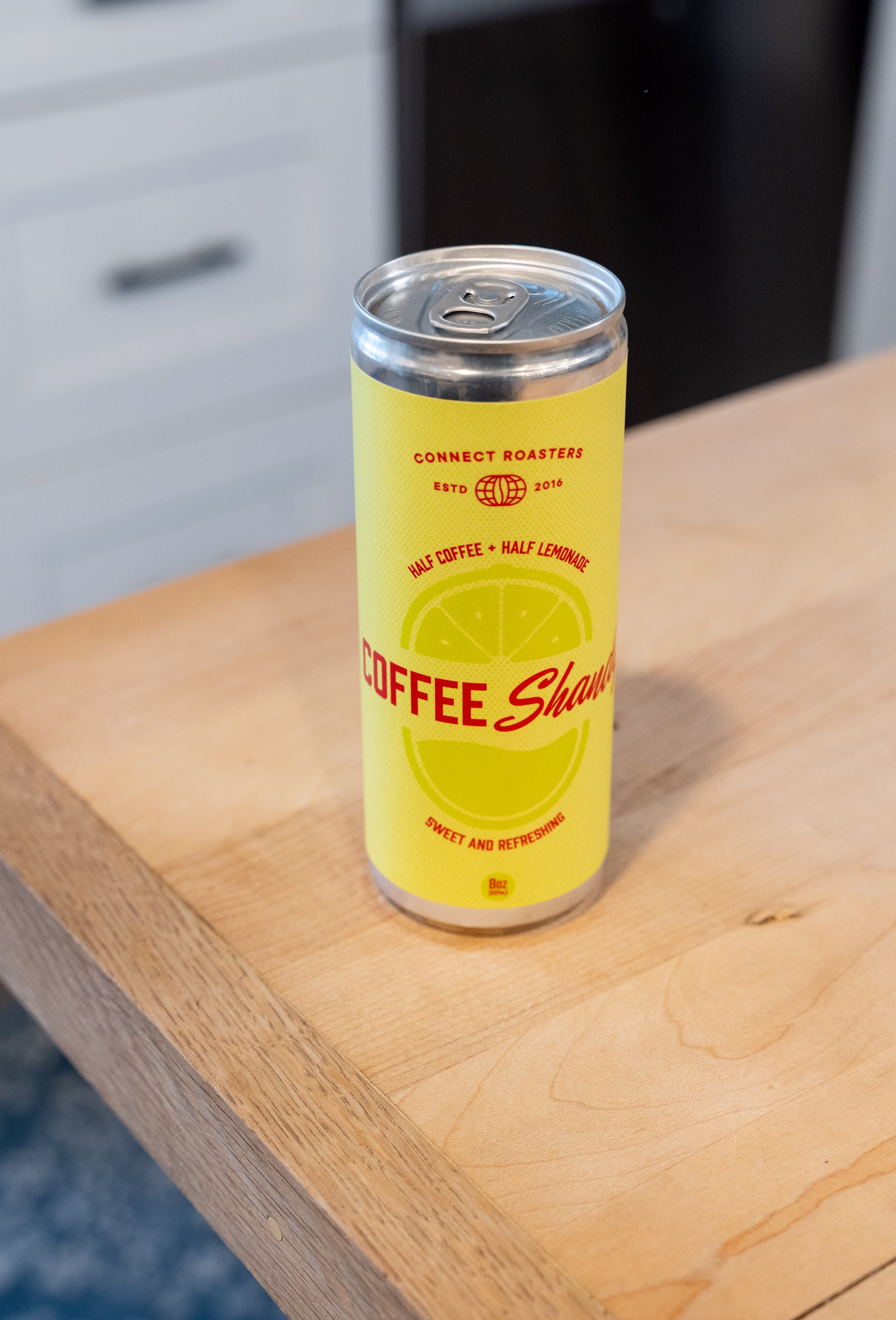 A tall can of coffee drink with a yellow label featuring a lime slice, placed on a wooden surface.