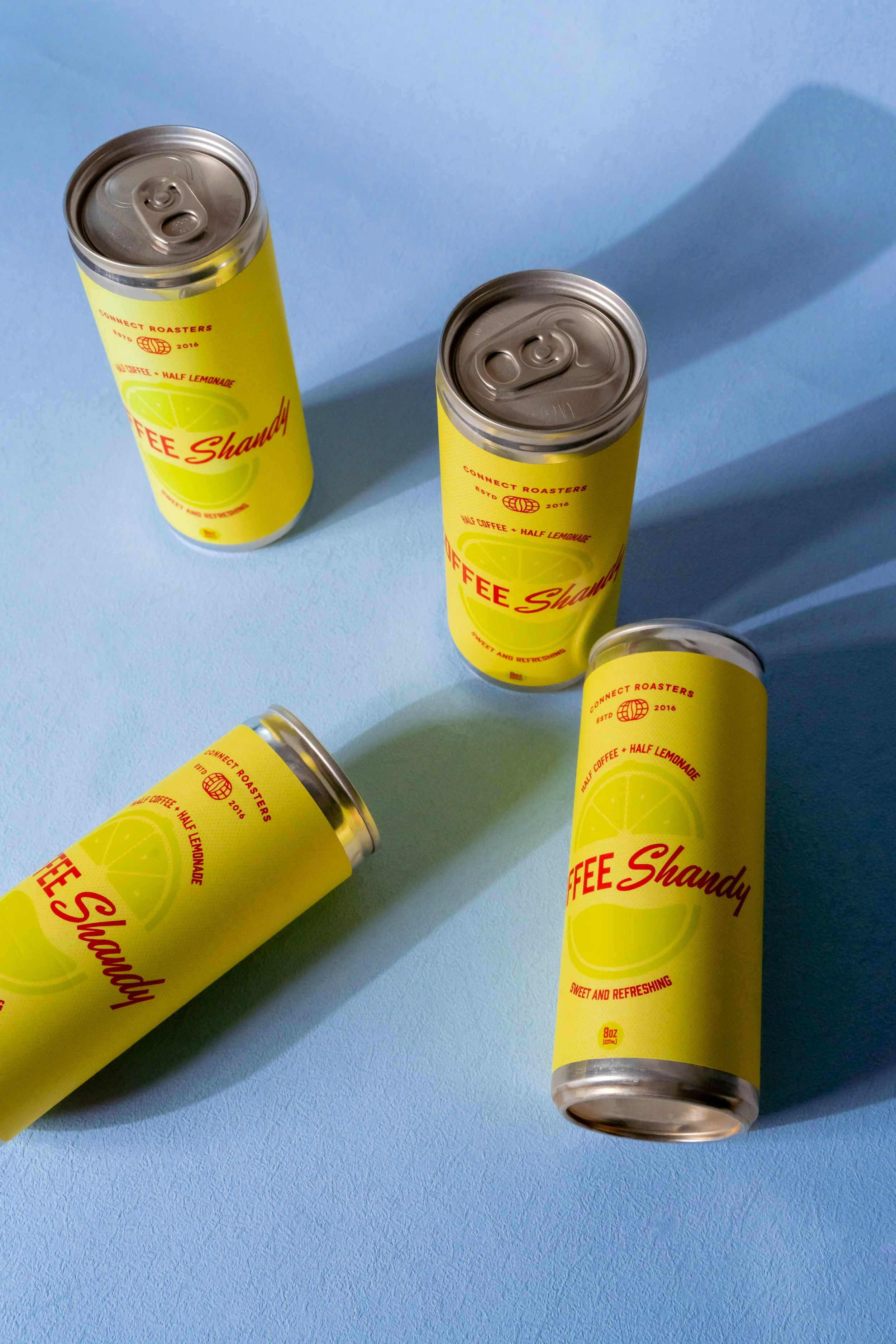 Four yellow cans of coffee and lemonade drink with silver tops on a blue surface, casting shadows.