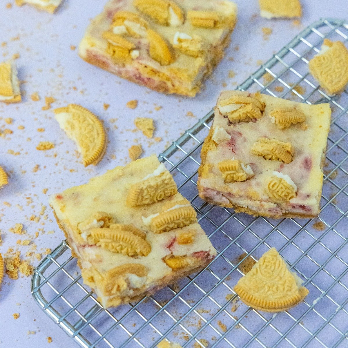 Frozen Oreo and cheese dessert bars with crushed cookies and whole Oreos on top, cooling on a wire rack with scattered crumbs around.