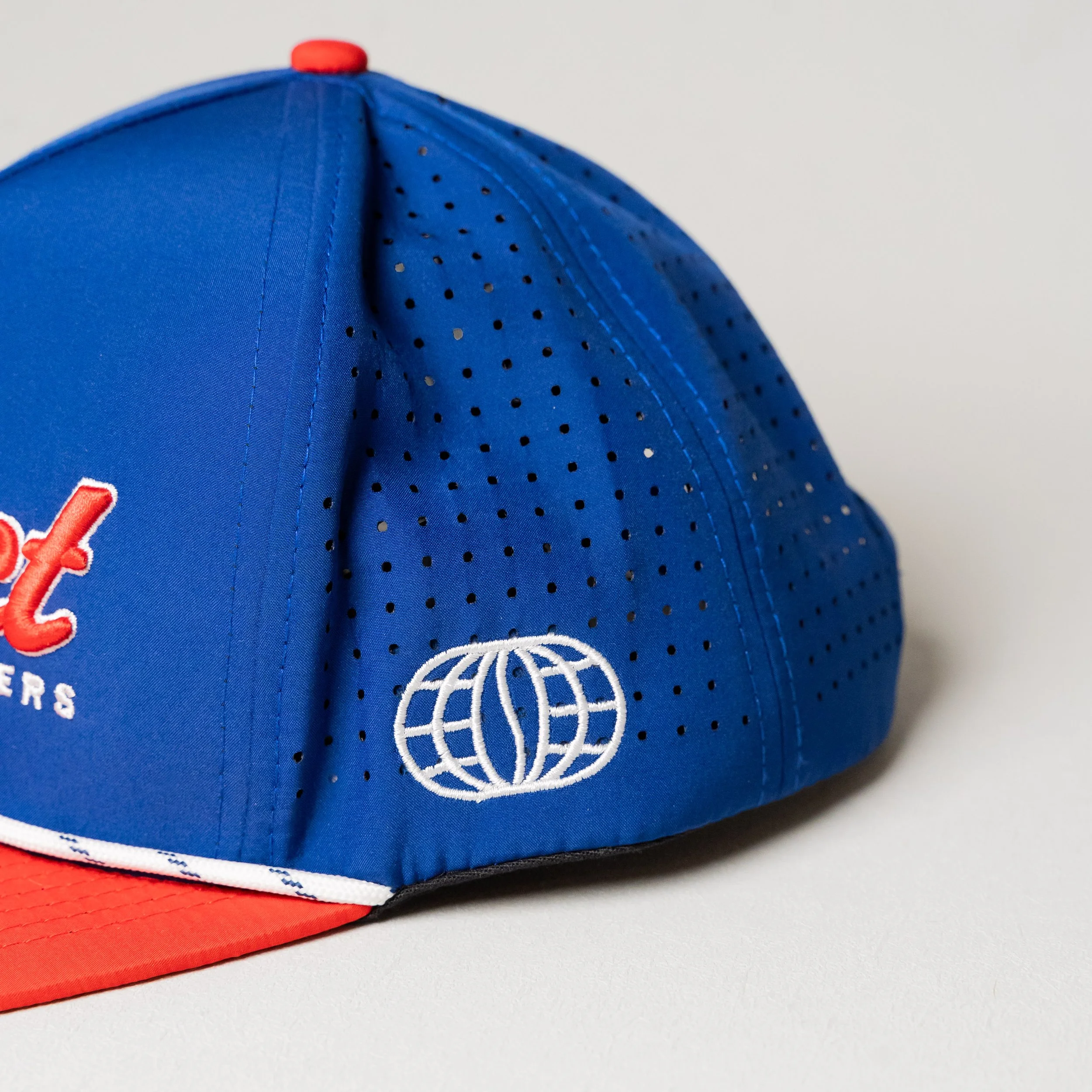 A blue baseball cap with a red brim, featuring embroidered white logo of a globe and partially visible text.