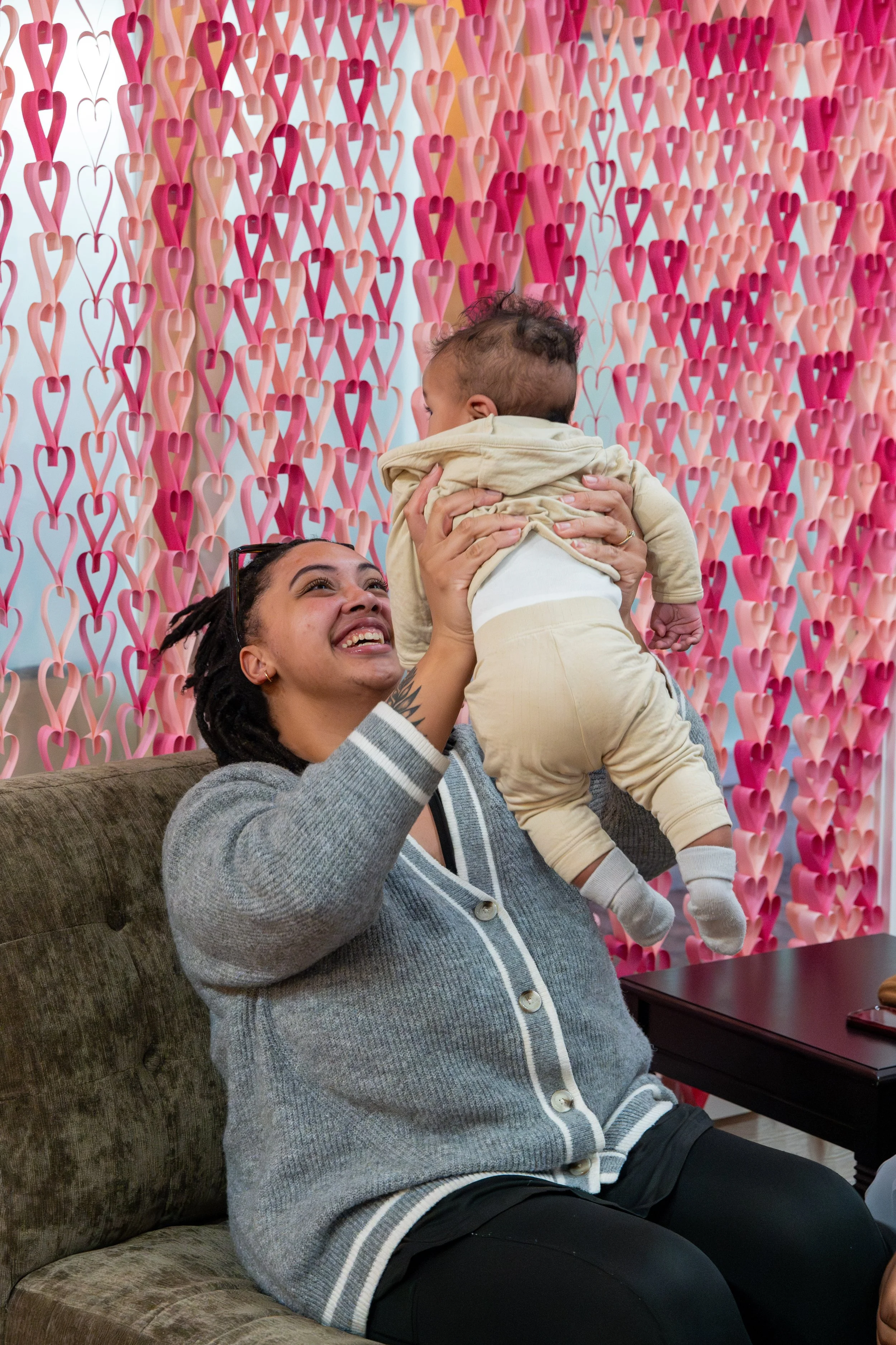 Woman lifting a baby in front of a wall decorated with pink and red paper hearts.