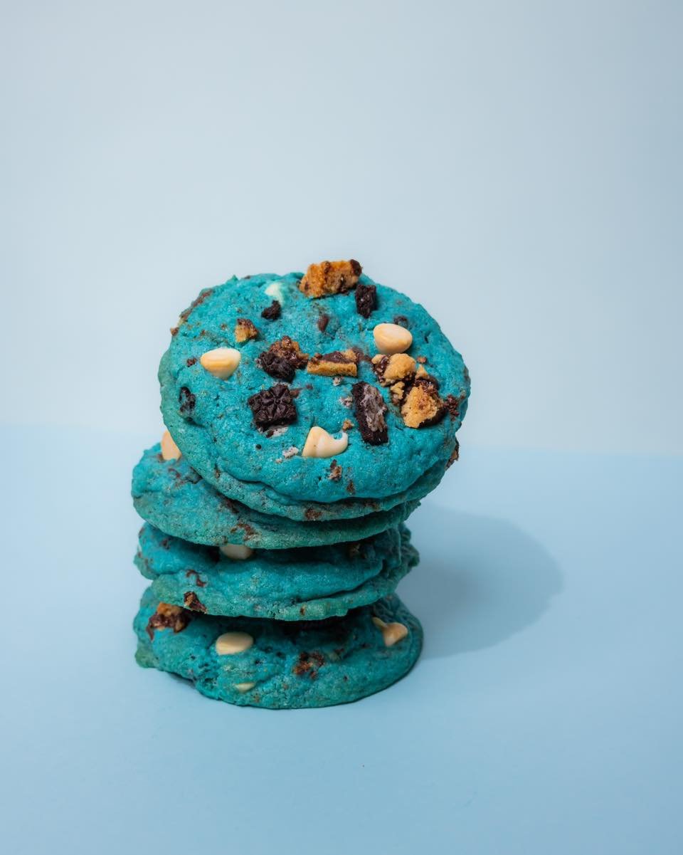 A stack of four blue cookies with white chocolate chips and chocolate chunks on a light blue background.