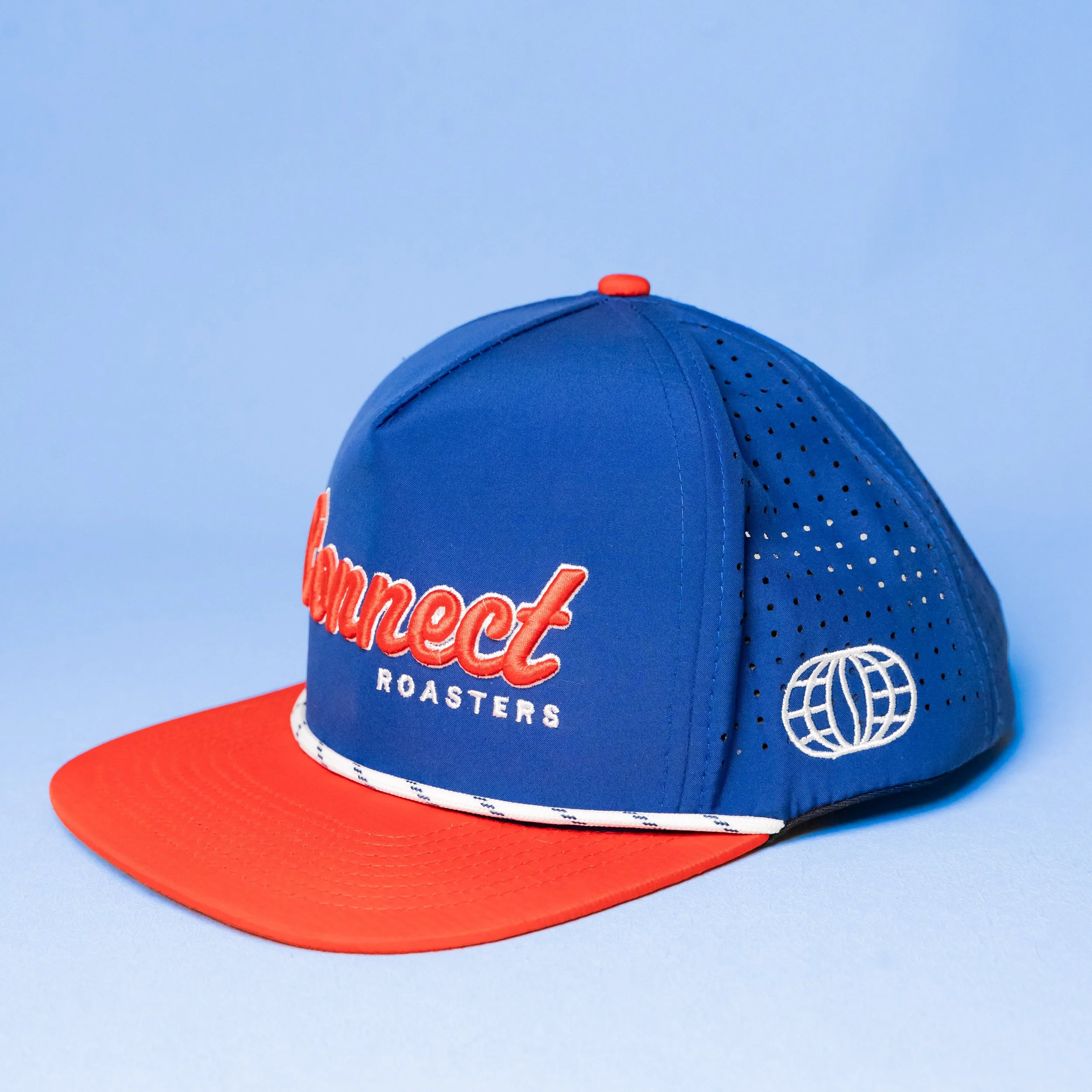 A blue and orange baseball cap with the words 'Connect Roasters' embroidered on the front and a globe logo on the side, against a light blue background.