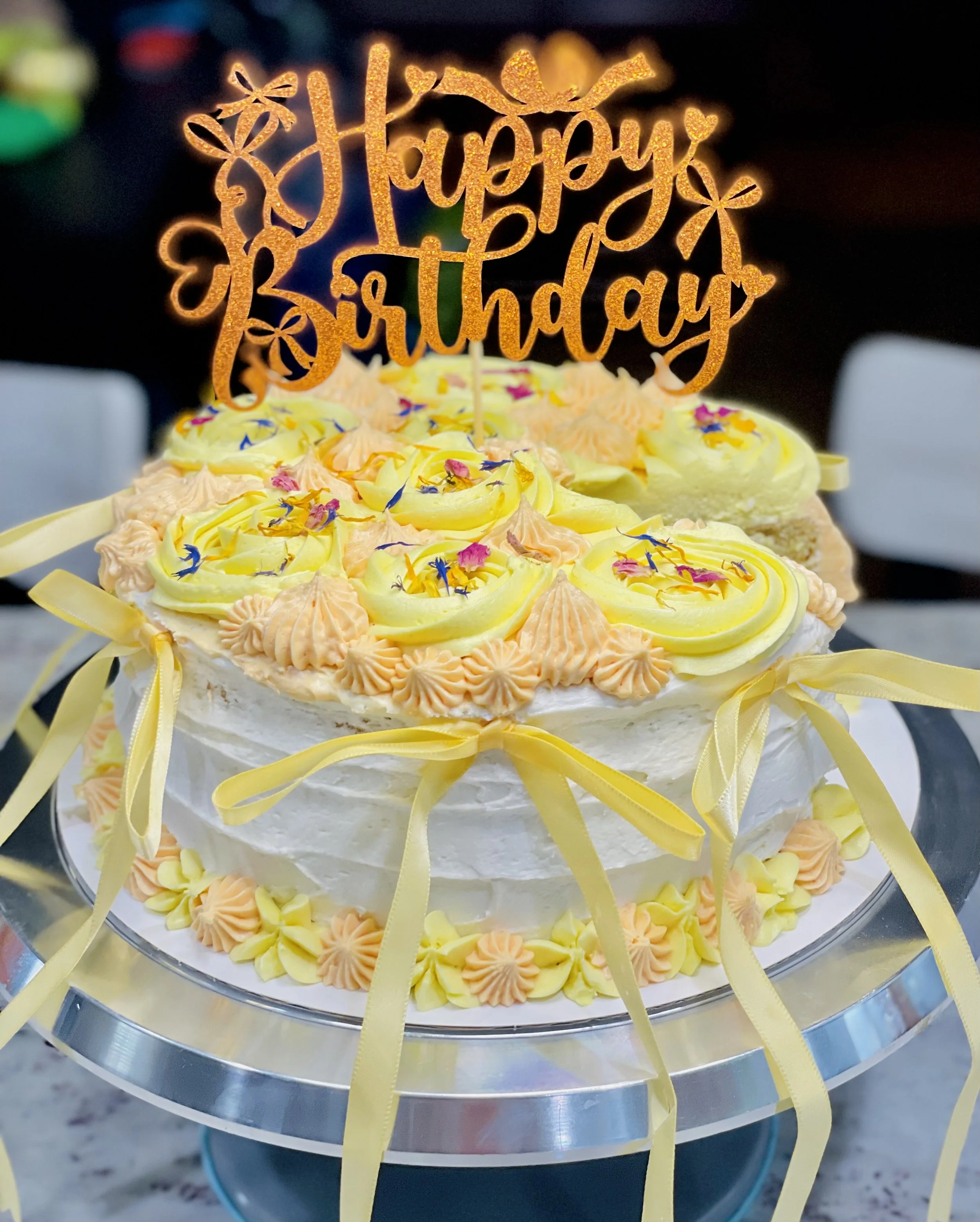 Vegan Citrus Blossom Cake – tropical pineapple coconut lemon curd cake topped with yellow rosettes, edible flowers, and birthday topper, made by Sunshine & Bloom Bakery in South Florida.